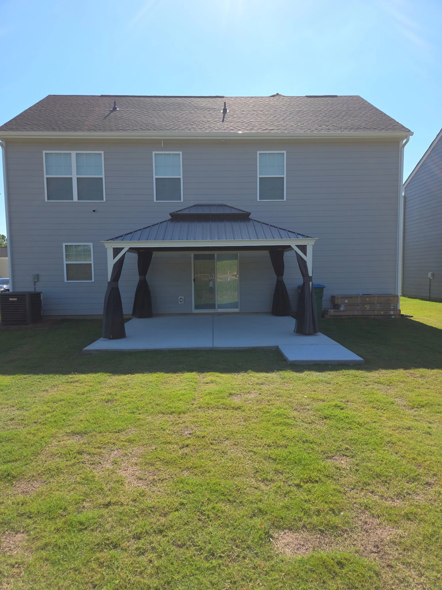Backyard of a house with a covered patio, green grass, and a blue sky