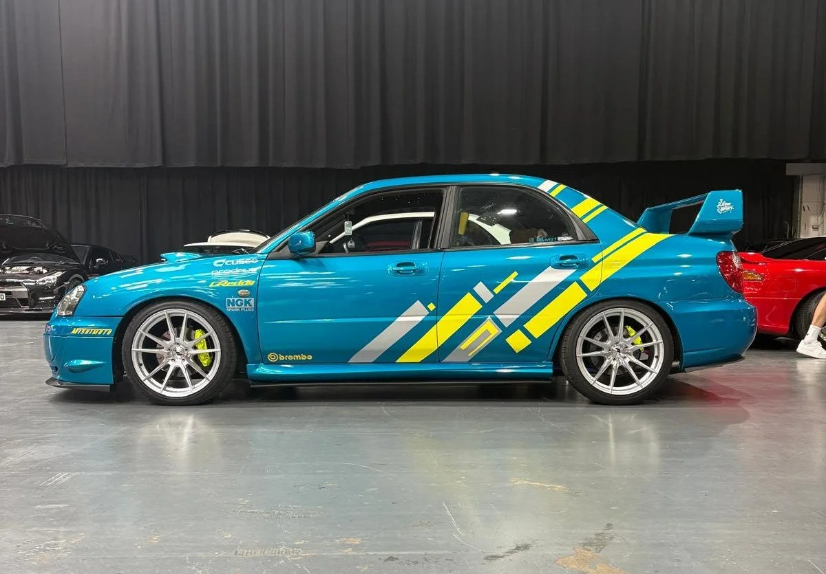 A blue race car with yellow and white graphics on the side, displayed indoors at a car show.