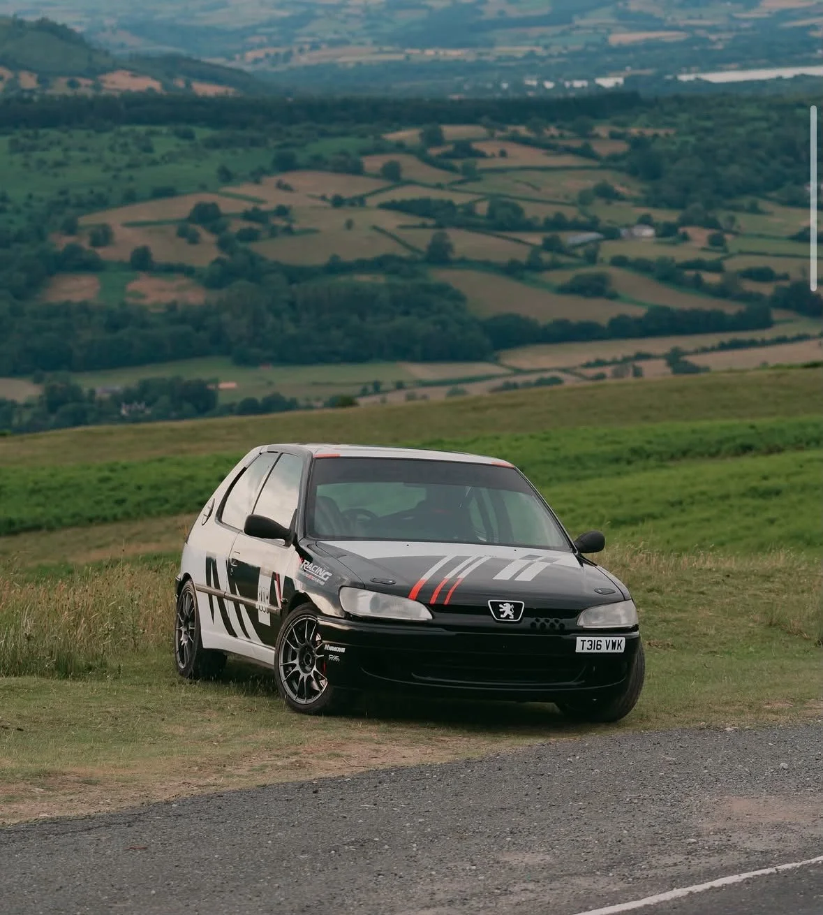 A black and white rally car with red accents parked on a grassy field with rolling hills in the background.