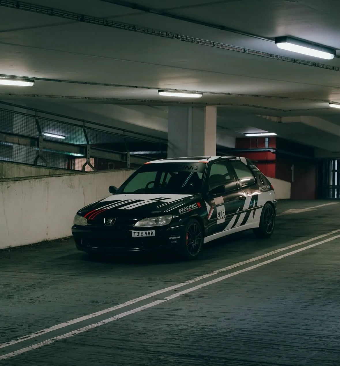 Black and white race car parked in a parking garage under artificial lighting.