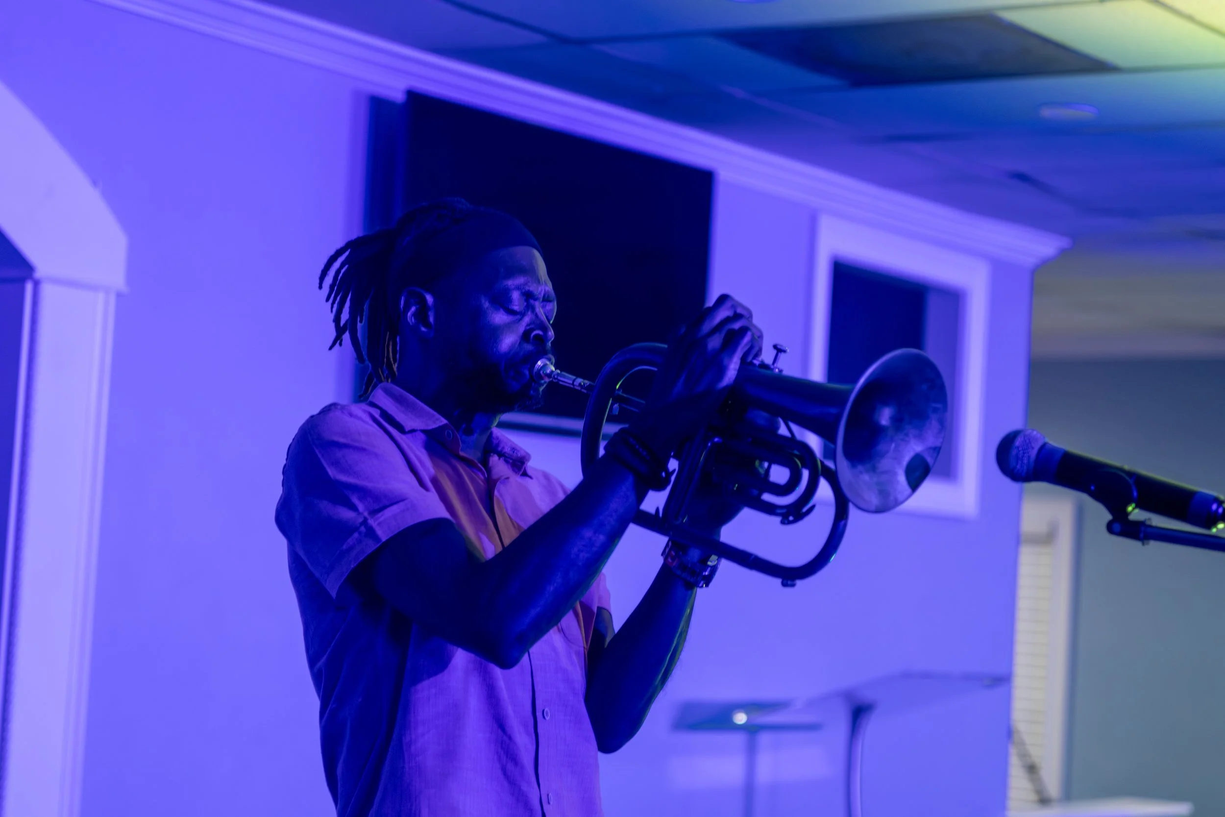 A man with dreadlocks playing a trumpet in a room with blue lighting.