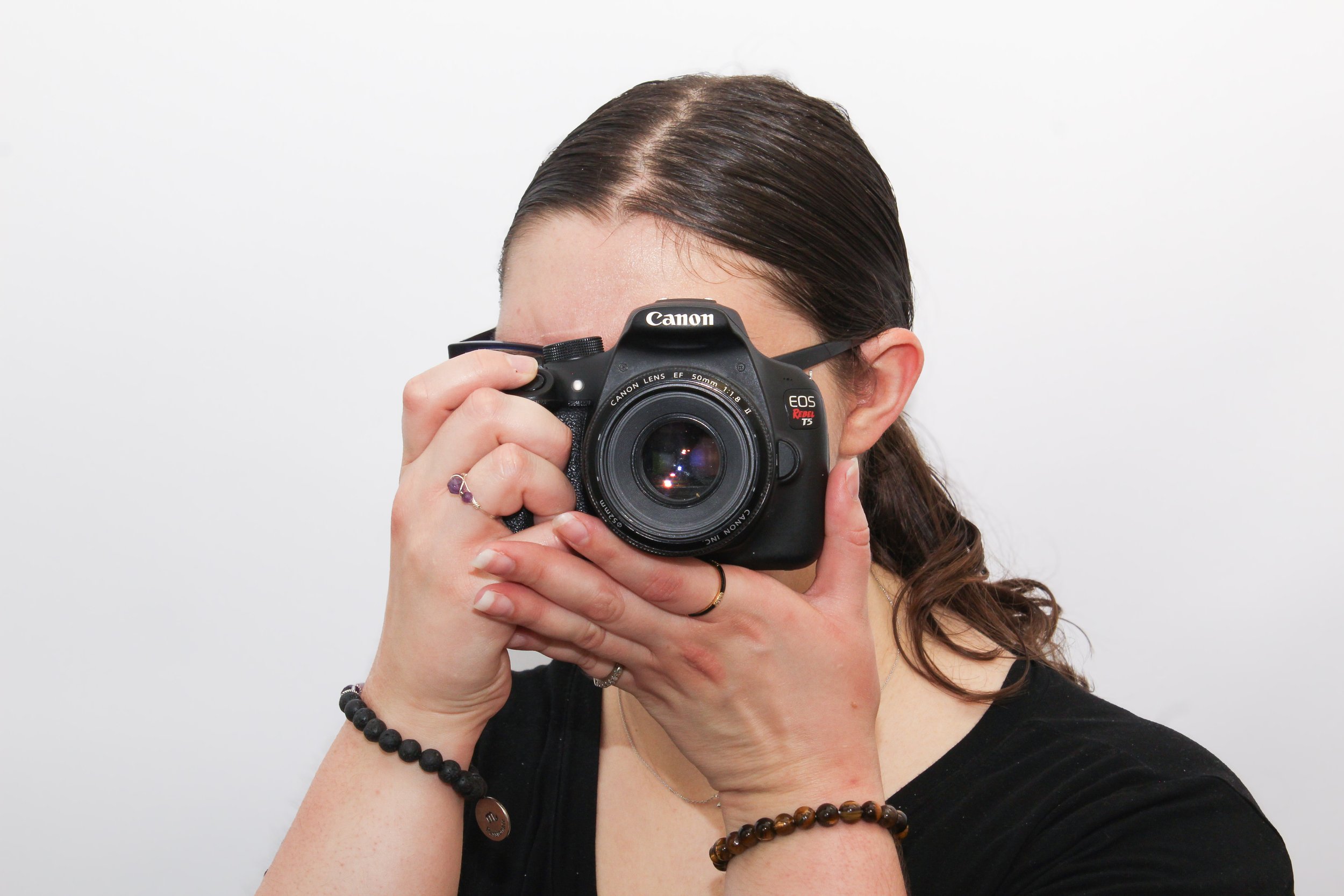 A woman with dark hair holding a Canon camera up to her face, taking a photo. She wears a black top, bracelets, and has a white background.
Located in Mesa, Arizona at Flash Haus