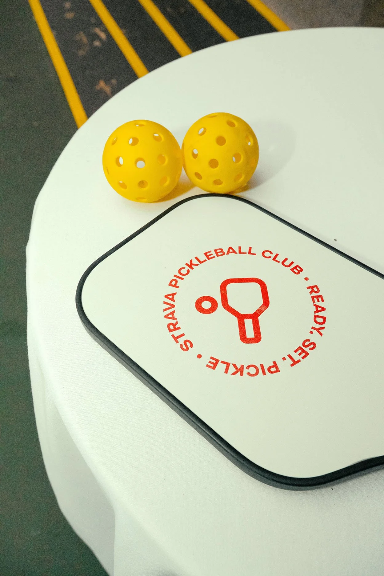 Two yellow perforated balls sitting on top of a white Surface Studio device with a red circular logo and text indicating the Strava Pickleball Club.