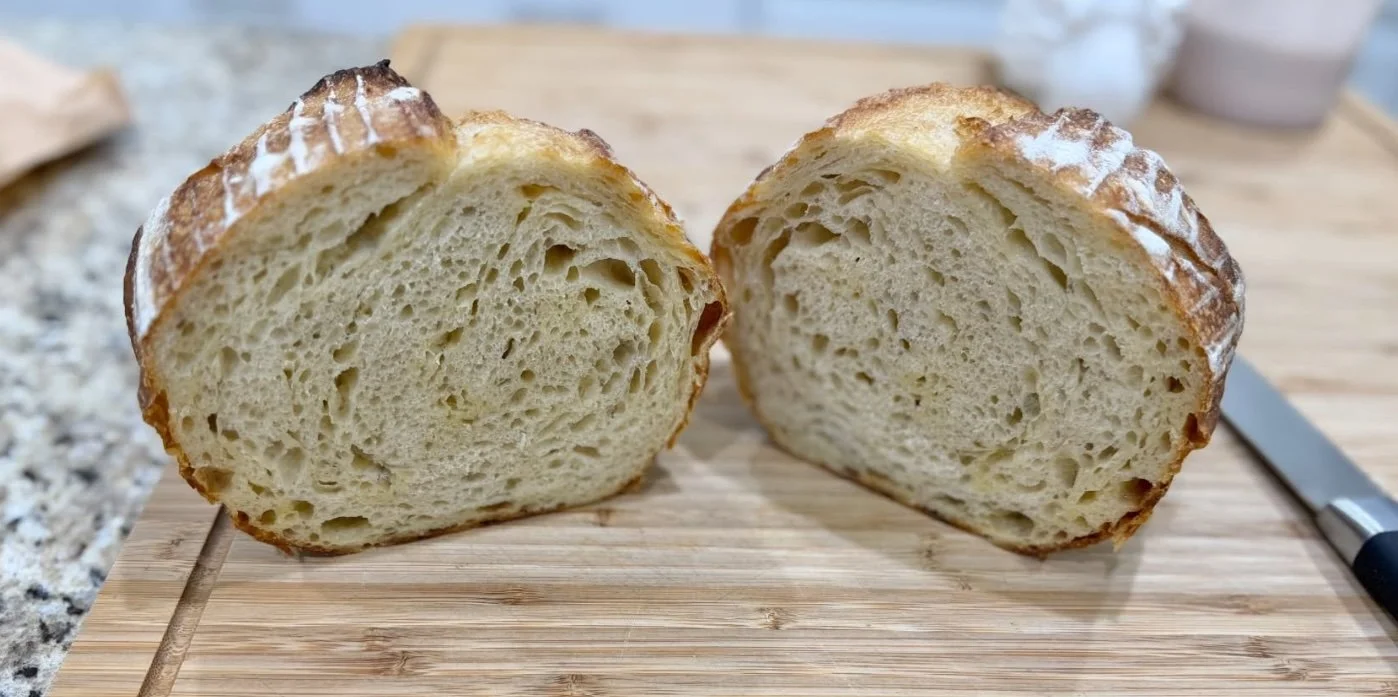 A loaf of bread cut in half on a wooden cutting board, with a knife nearby.