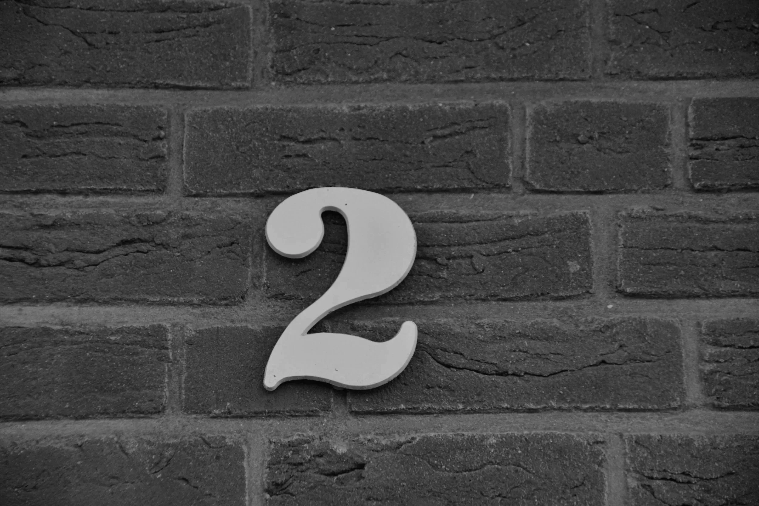 A white question mark decoration mounted on a dark brick wall.