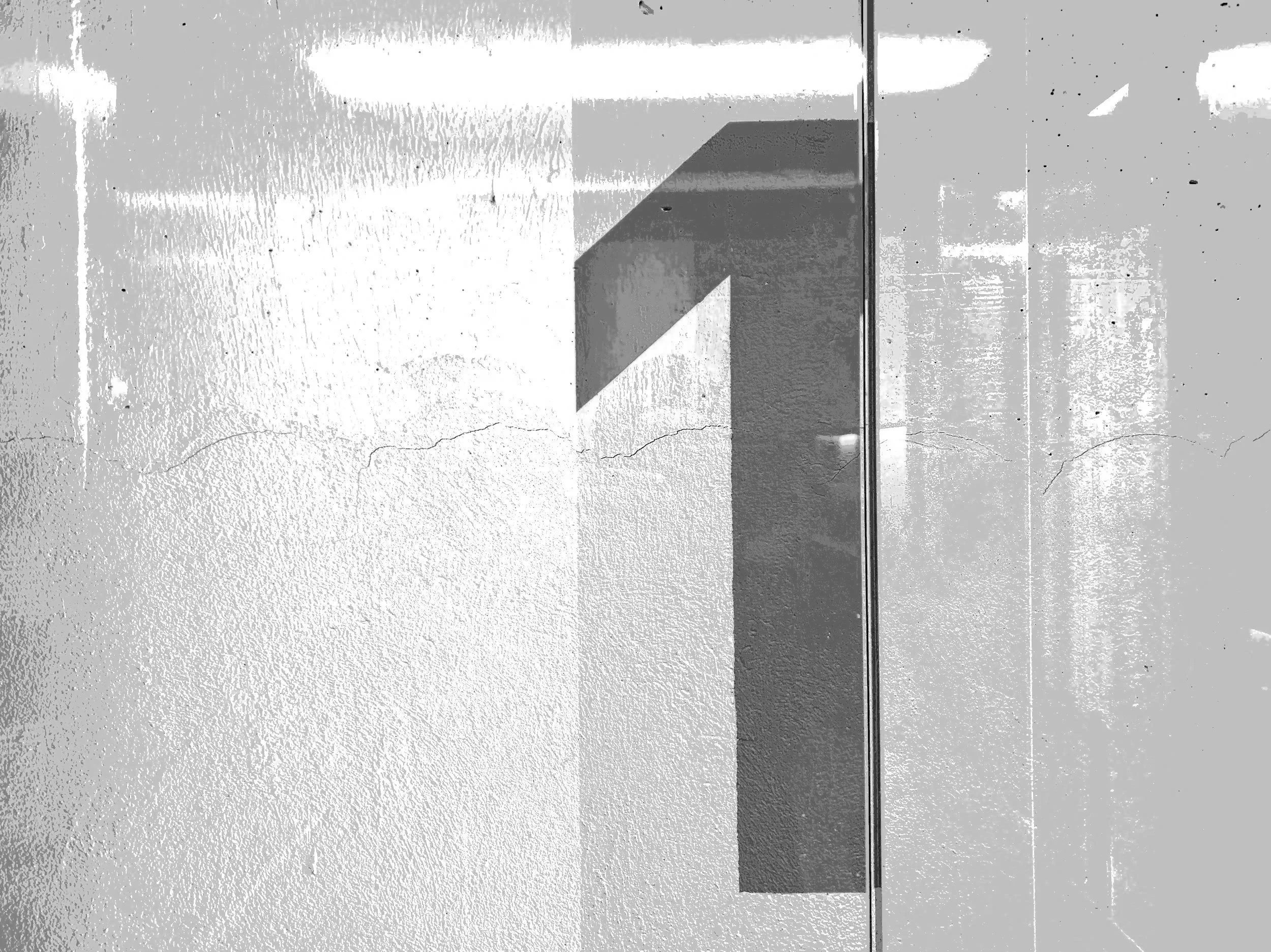 Black and white photo of an elevator door with a shadow cast on a textured wall beside it.