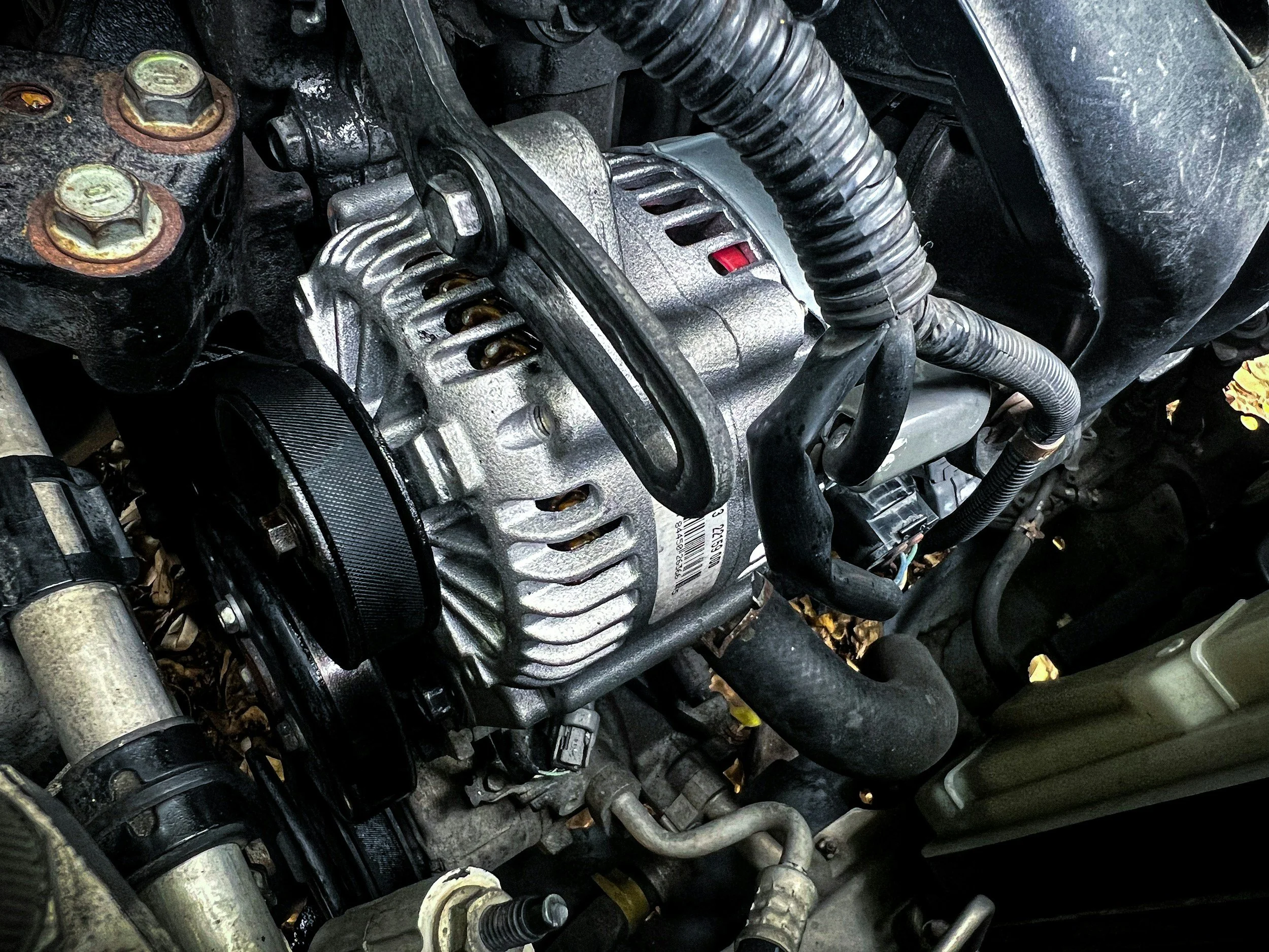 Close-up view of a car engine showing various components such as the alternator, hoses, bolts, and metallic parts.