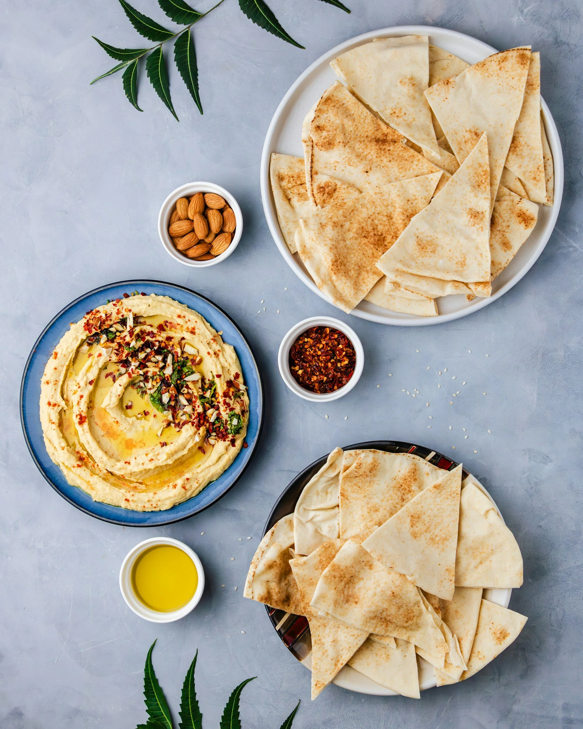 Overhead Mediterranean spread with hummus, pita bread, almonds, and chili oil.