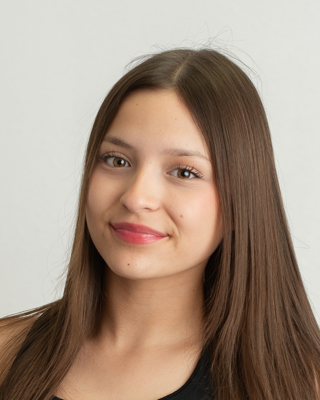 Portrait of a young woman with long brown hair and light makeup smiling softly against a plain white background.