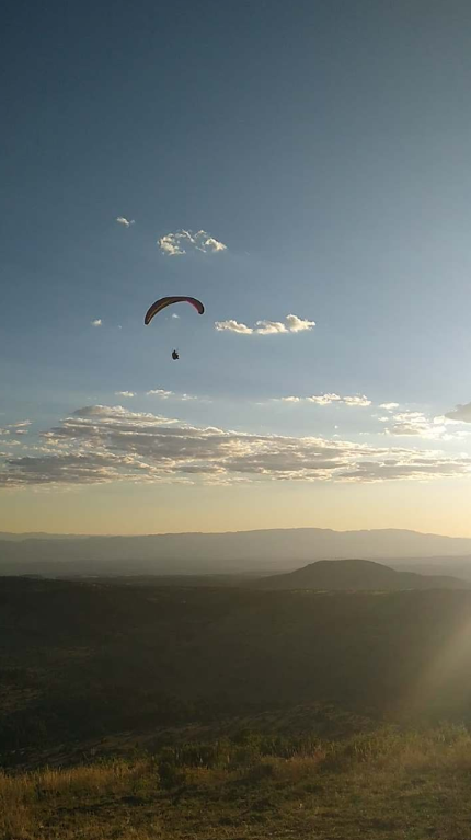 Paraglider flying in the sky during sunset over a hilly landscape with scattered clouds.