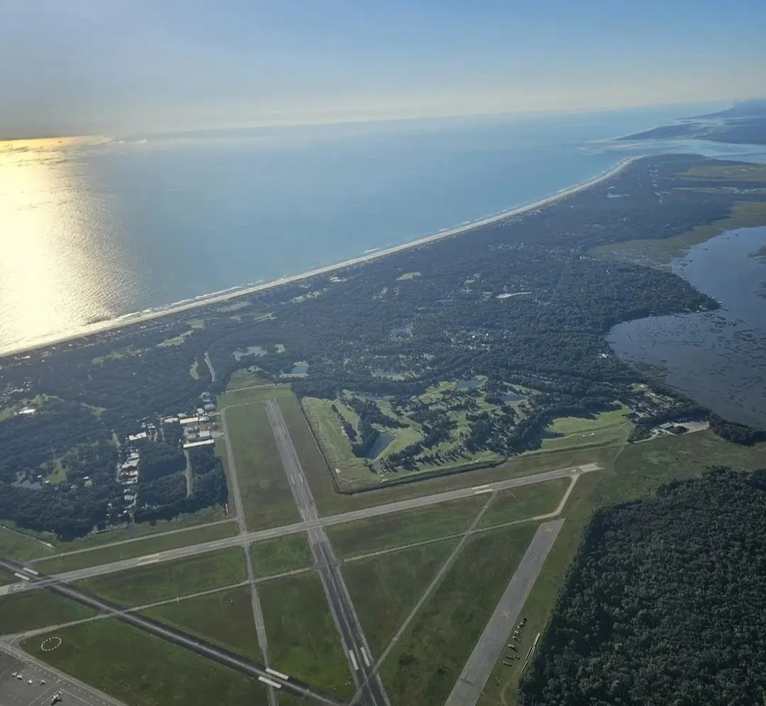 Aerial view of an airport near a large body of water, with runways, taxiways, and surrounding greenery.