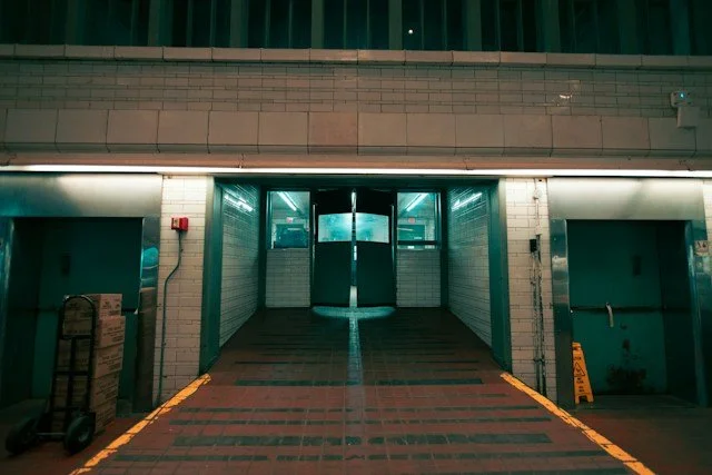 Industrial or commercial building entrance with open double doors, brick walls, and an emergency exit sign.