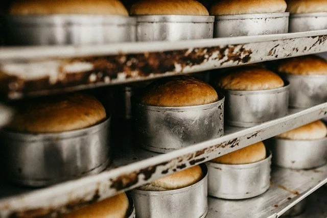 Baked bread rising in metal molds on a metal rack in a bakery.