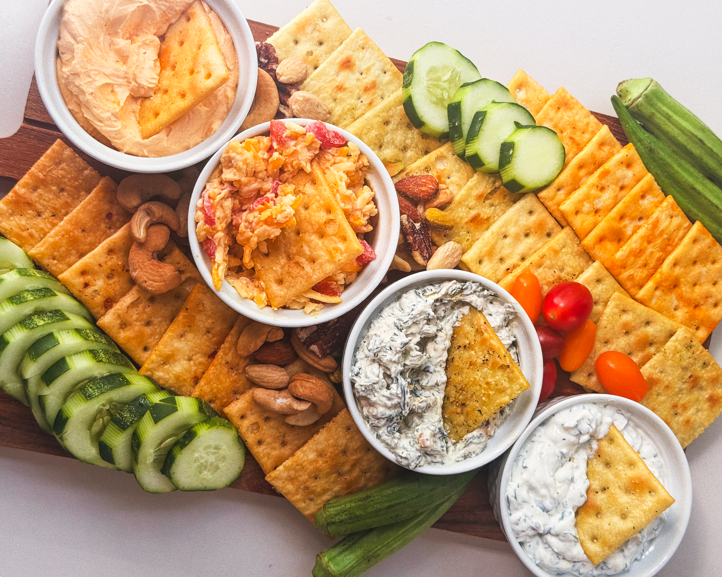 Assorted dips, crackers, and vegetables arranged on a wooden platter.