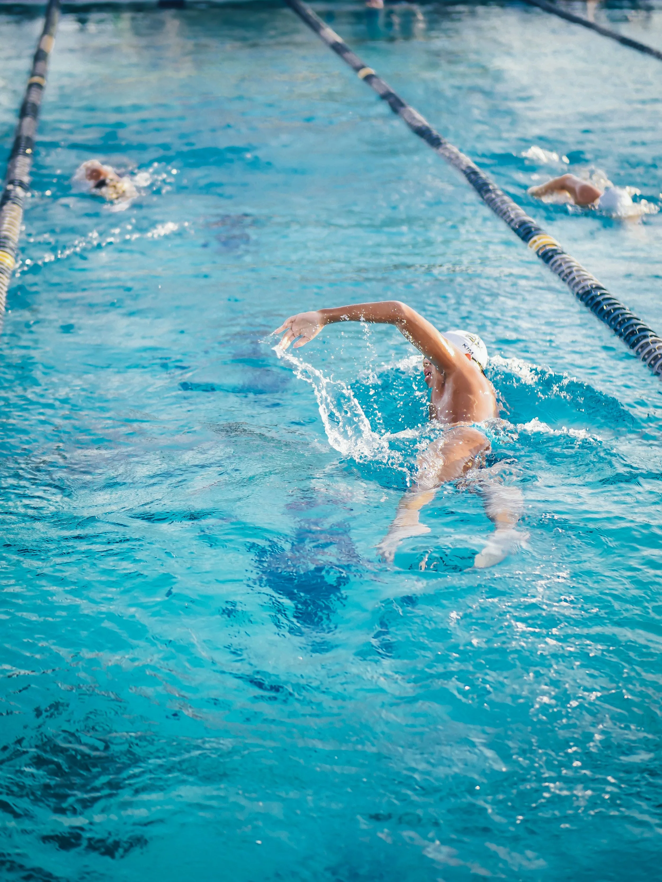 Swimmer performing a backstroke in a swimming pool, with lane dividers visible.