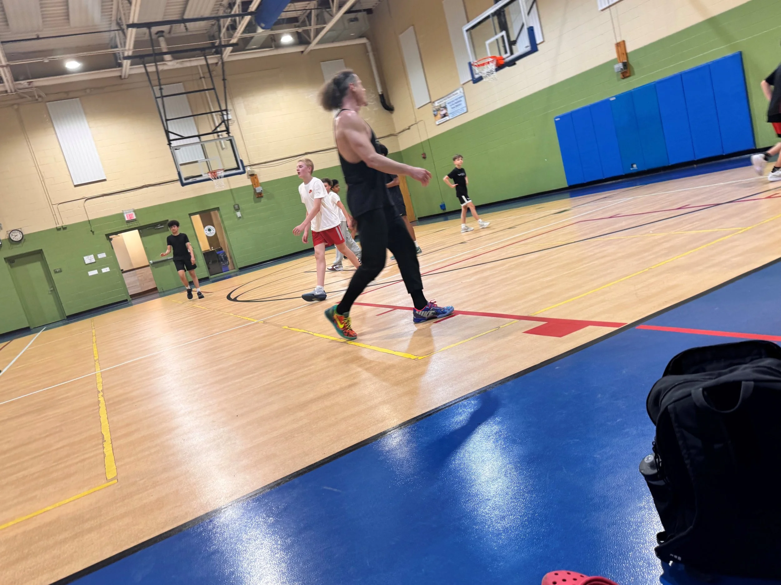 People playing basketball in a gymnasium, some are shooting hoops and others are standing or walking around.