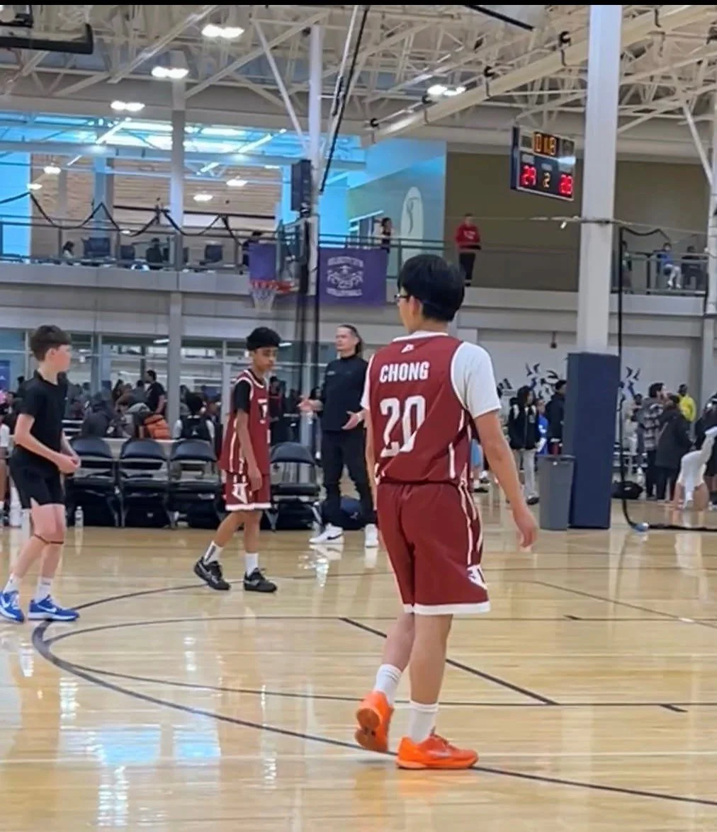 A youth basketball game taking place indoors at a gym, with players on the court and spectators in the background.