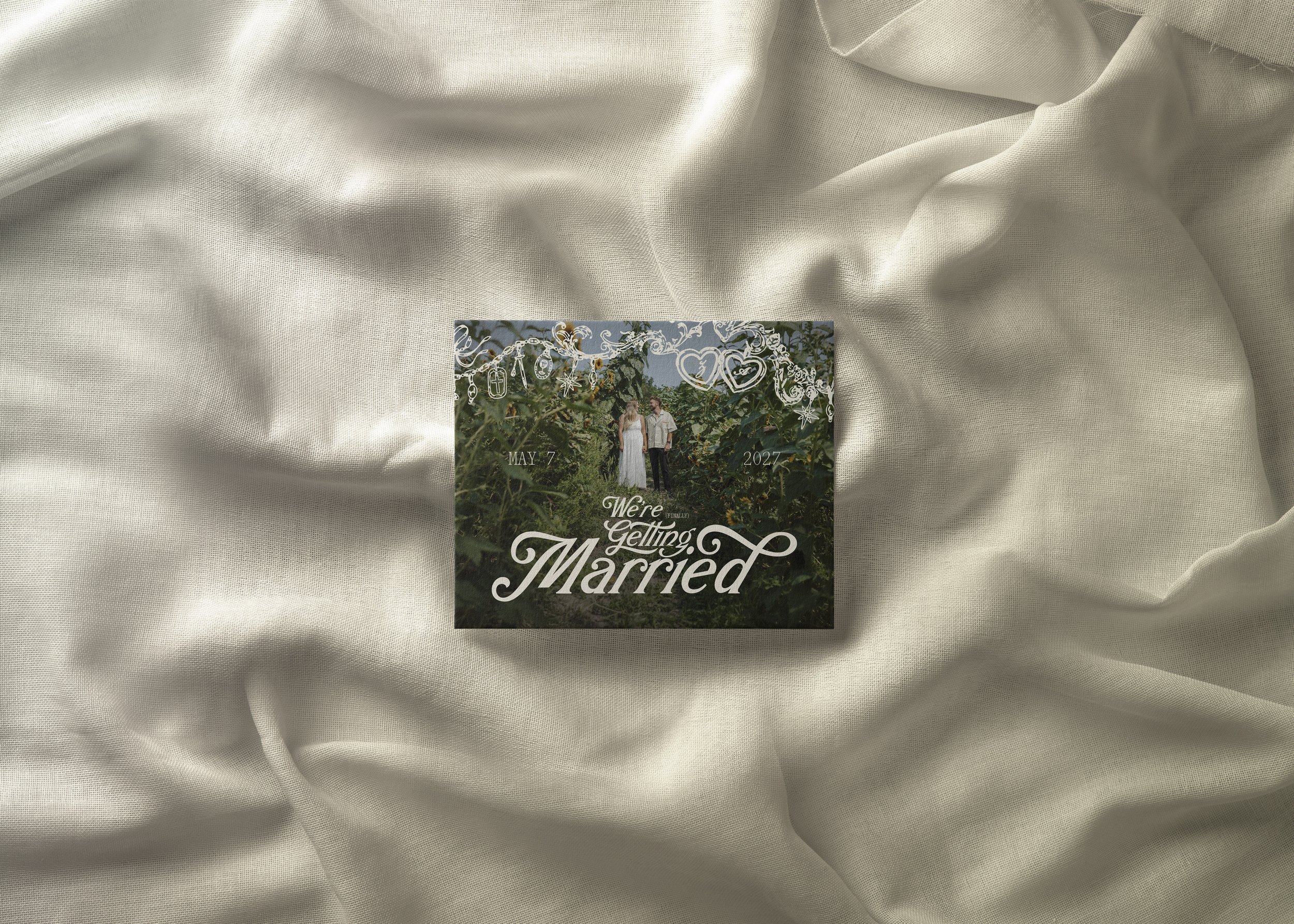Wedding announcement card with a couple outdoors, white decorative elements, and text 'We're Gelling Married' placed on off-white fabric.