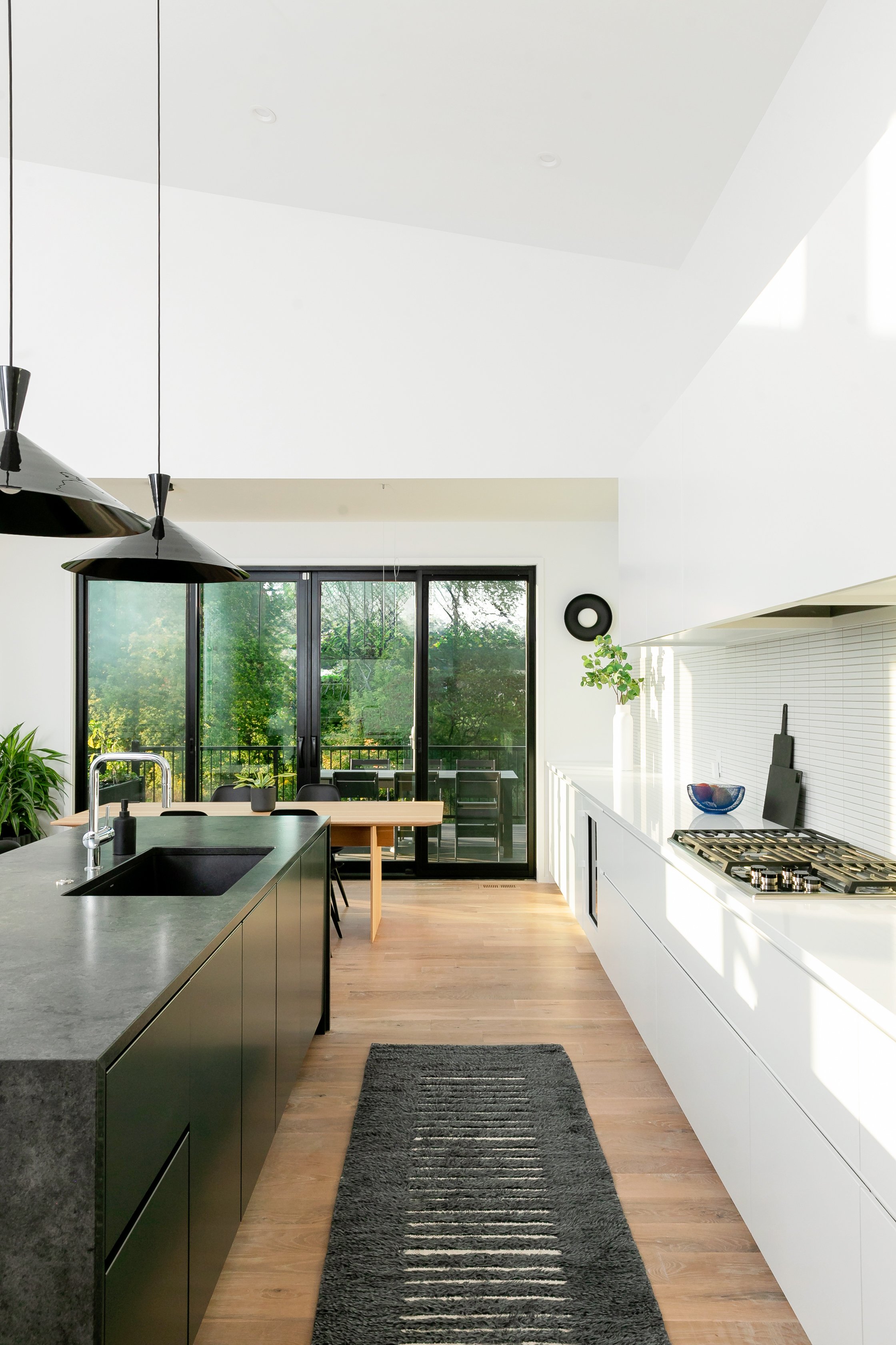 Modern kitchen with black island, white cabinets, and large glass sliding doors to outdoor space, with a black pendant light and some plants