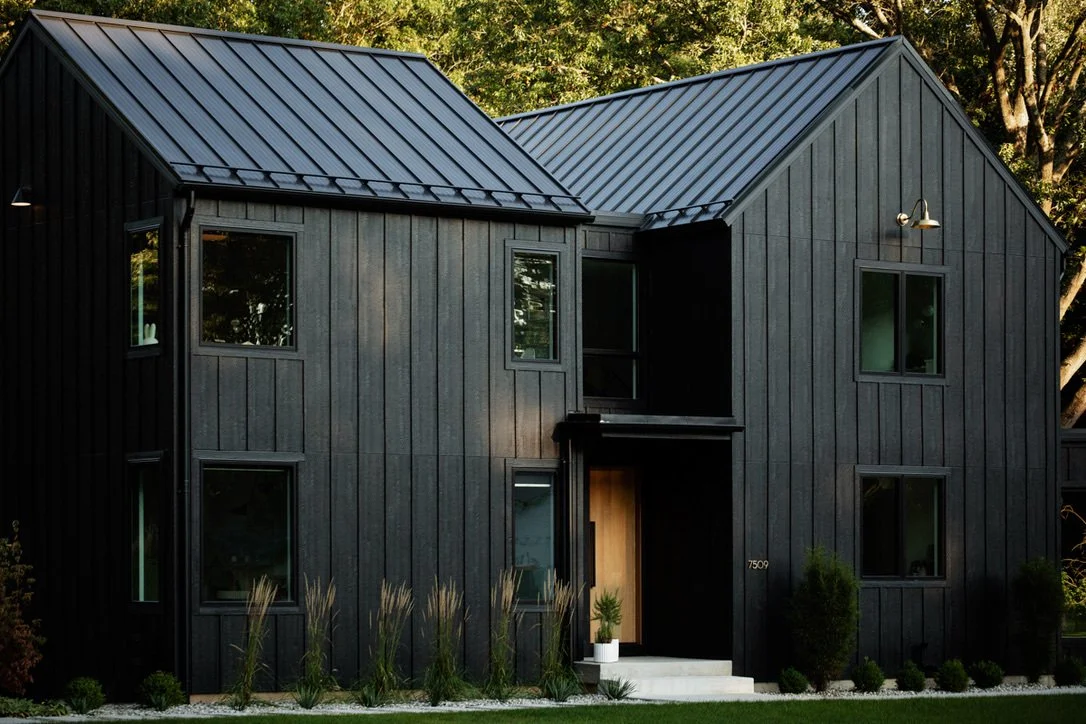 A modern black two-story house with a metal roof, several windows, and minimal landscaping in front.