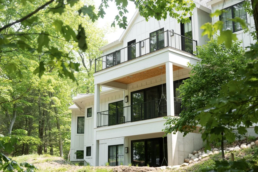 Modern multi-story house with balconies, surrounded by trees and greenery