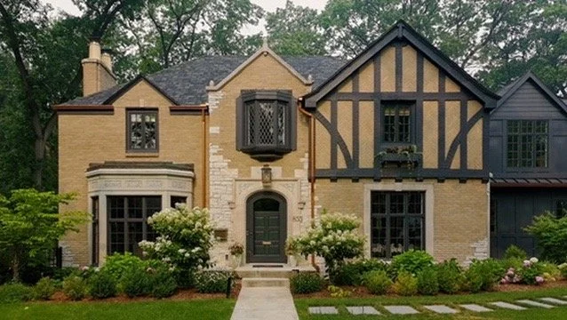 Front view of a two-story house with a mix of brick and Tudor-style black timber framing, surrounded by a well-maintained garden and pathway.