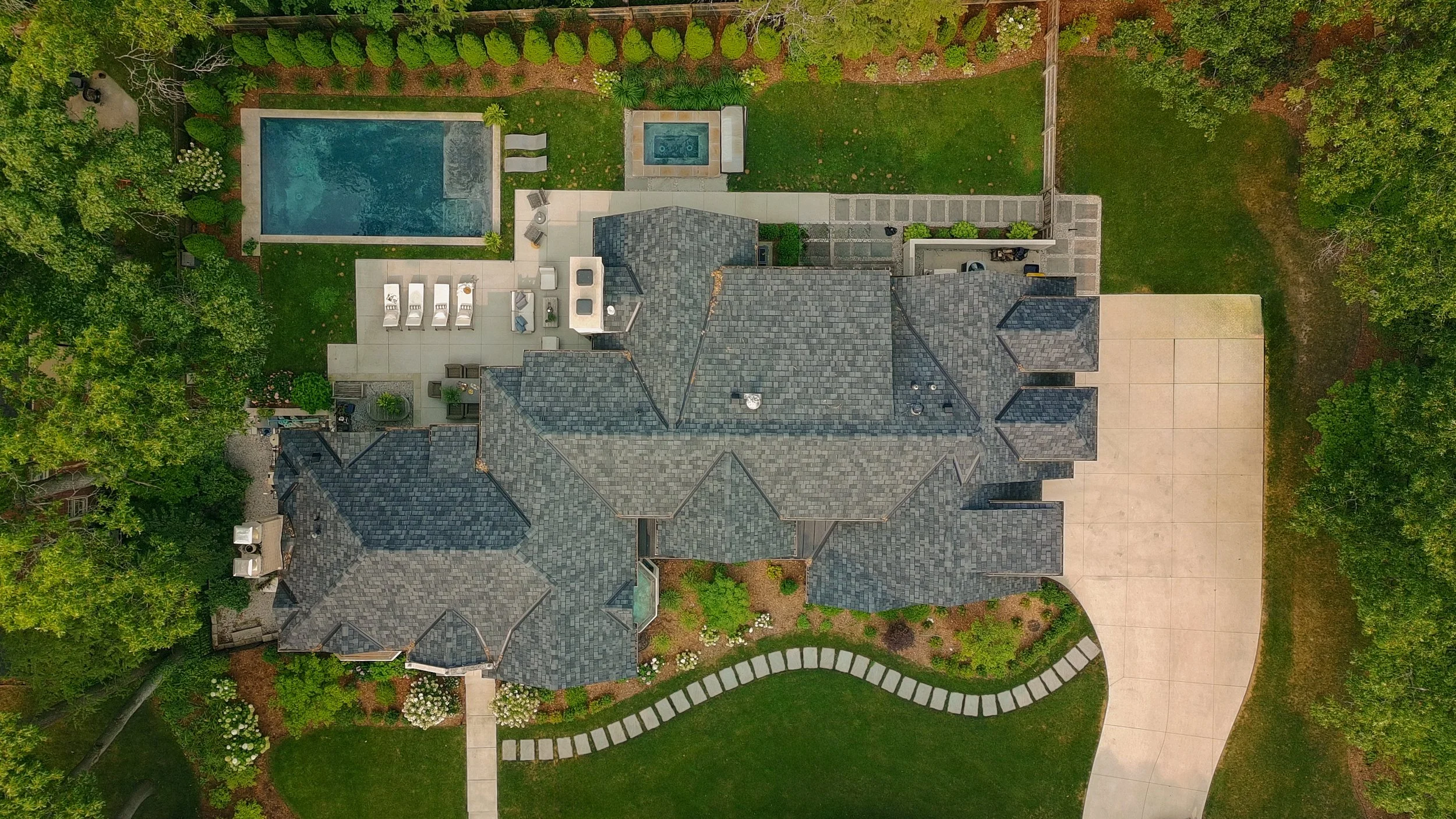 An overhead view of a large house, backyard, swimming pool, hot tub, garden, trees, and pathways.