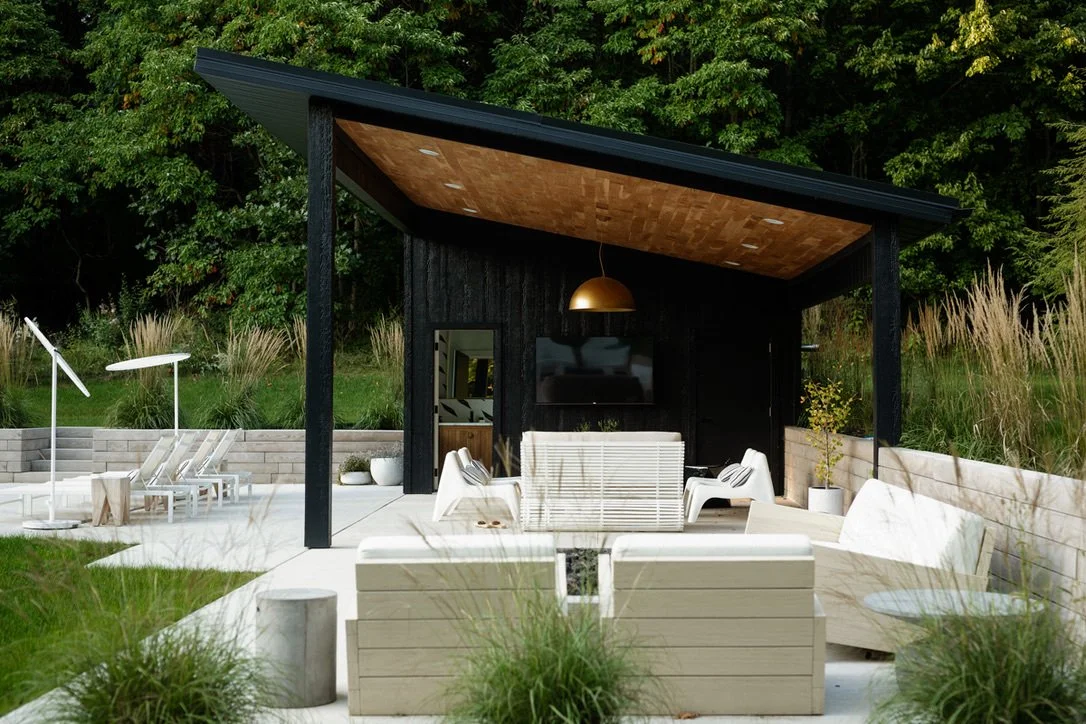 Outdoor patio with modern seating, a flat-screen TV, and a pitched roof, surrounded by trees and greenery.