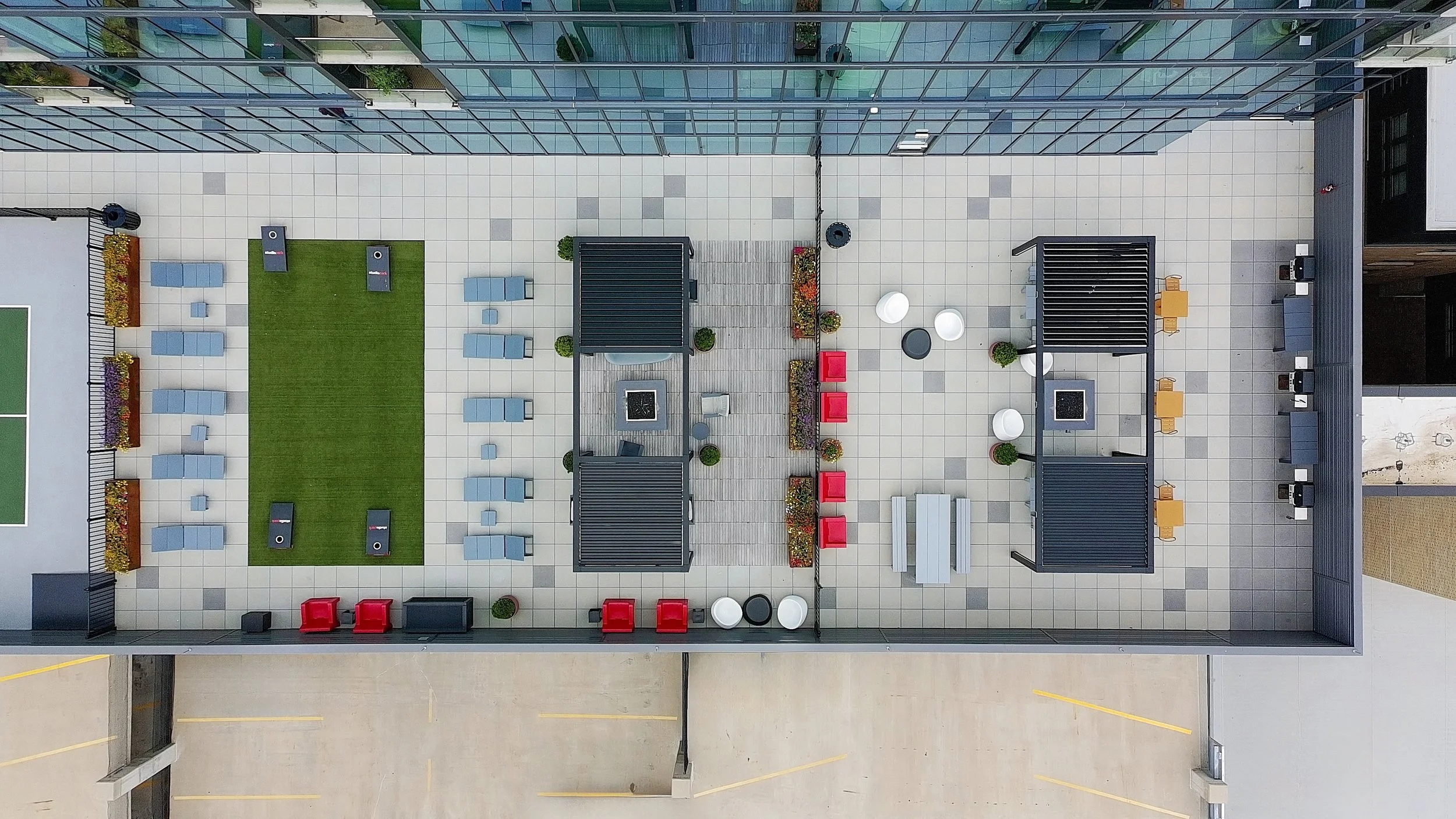 Top-down view of a modern rooftop patio area with grass, outdoor furniture, planters, and a surrounding glass building.
