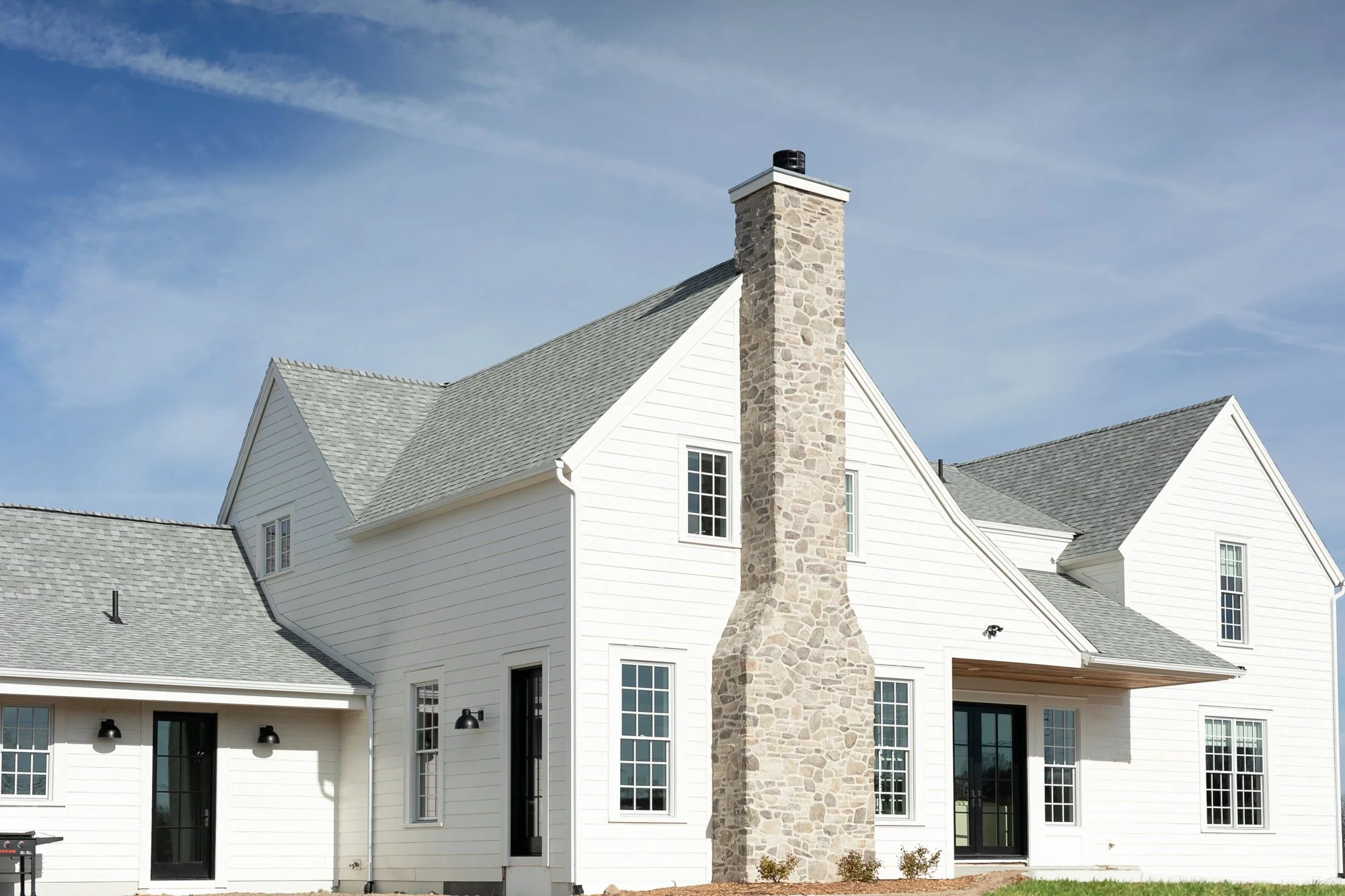 Exterior of a modern white house with a stone chimney and multiple windows under a partly cloudy sky.