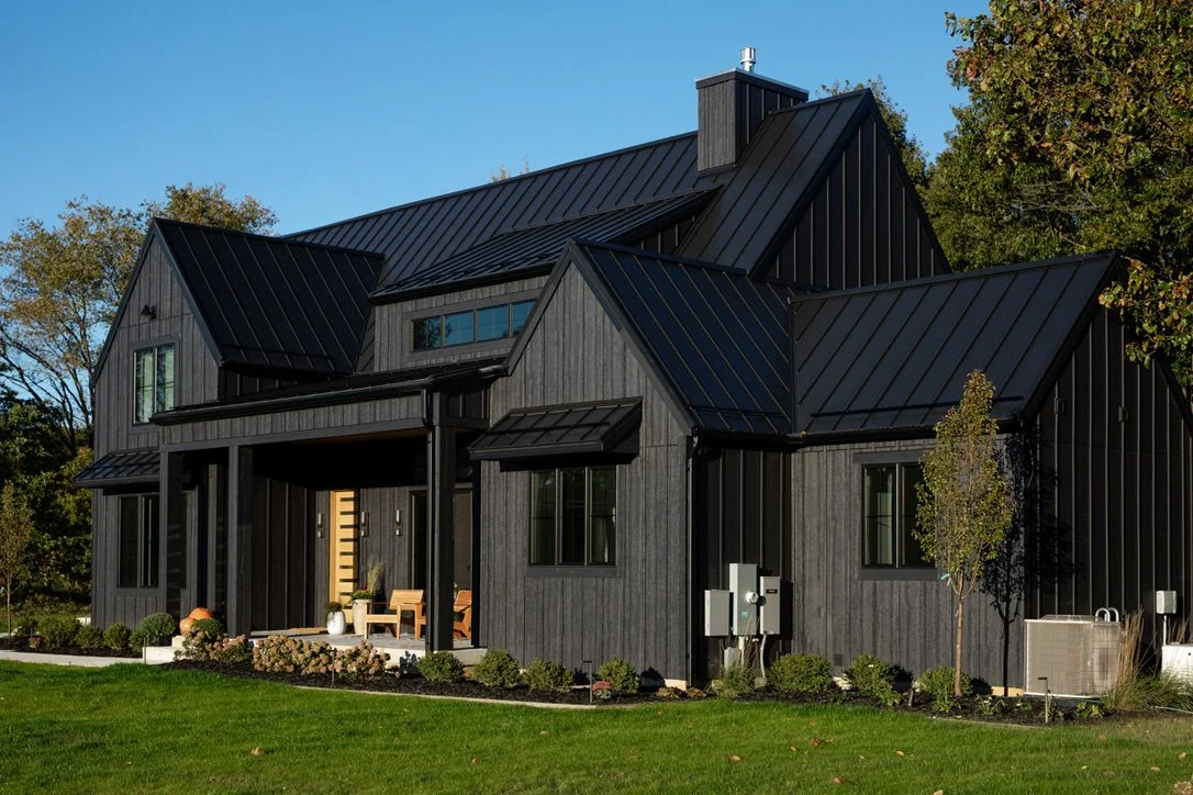 A modern black house with metal roofing, surrounded by a green lawn and trees.
