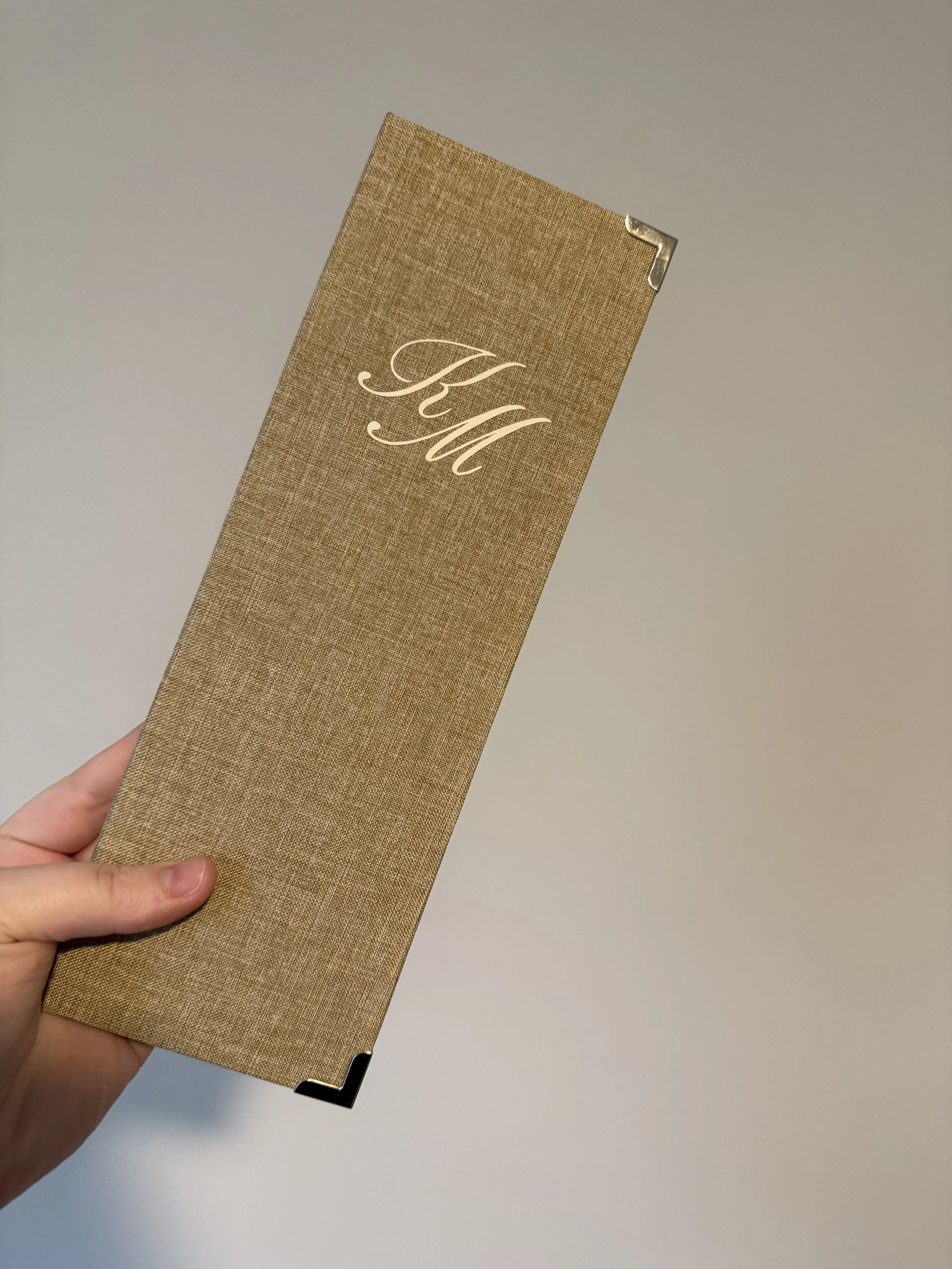 A hand holding a gold-colored card with a textured surface and the initials 'KW' in elegant white script.