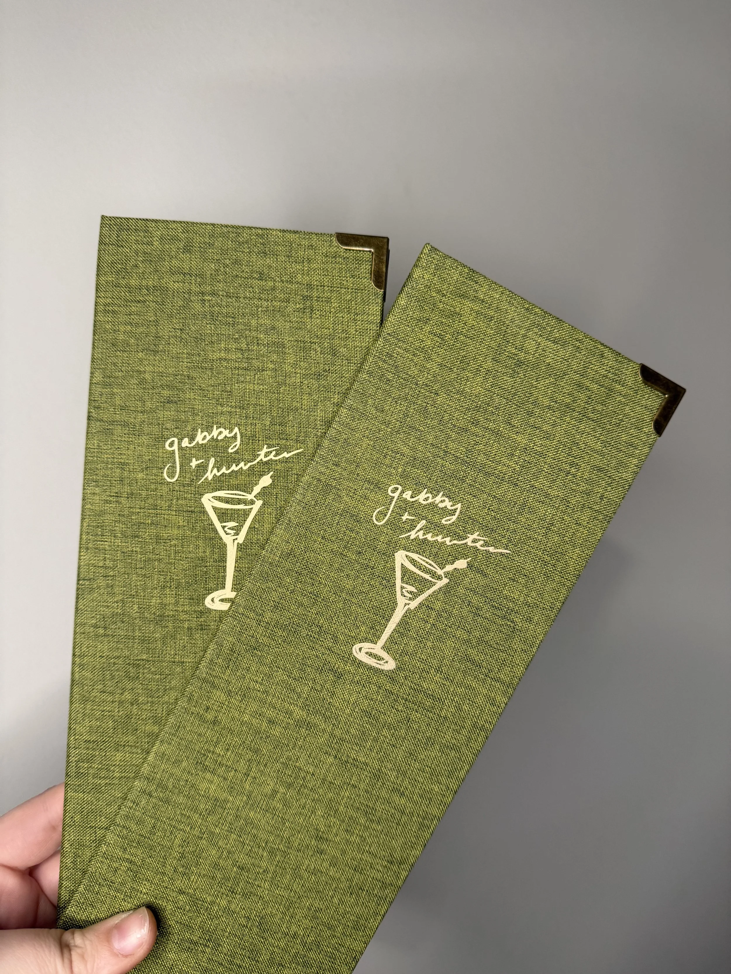 Two green cocktail napkins with white print of a martini glass and the phrase "gabbing + drinking" on a gray surface.