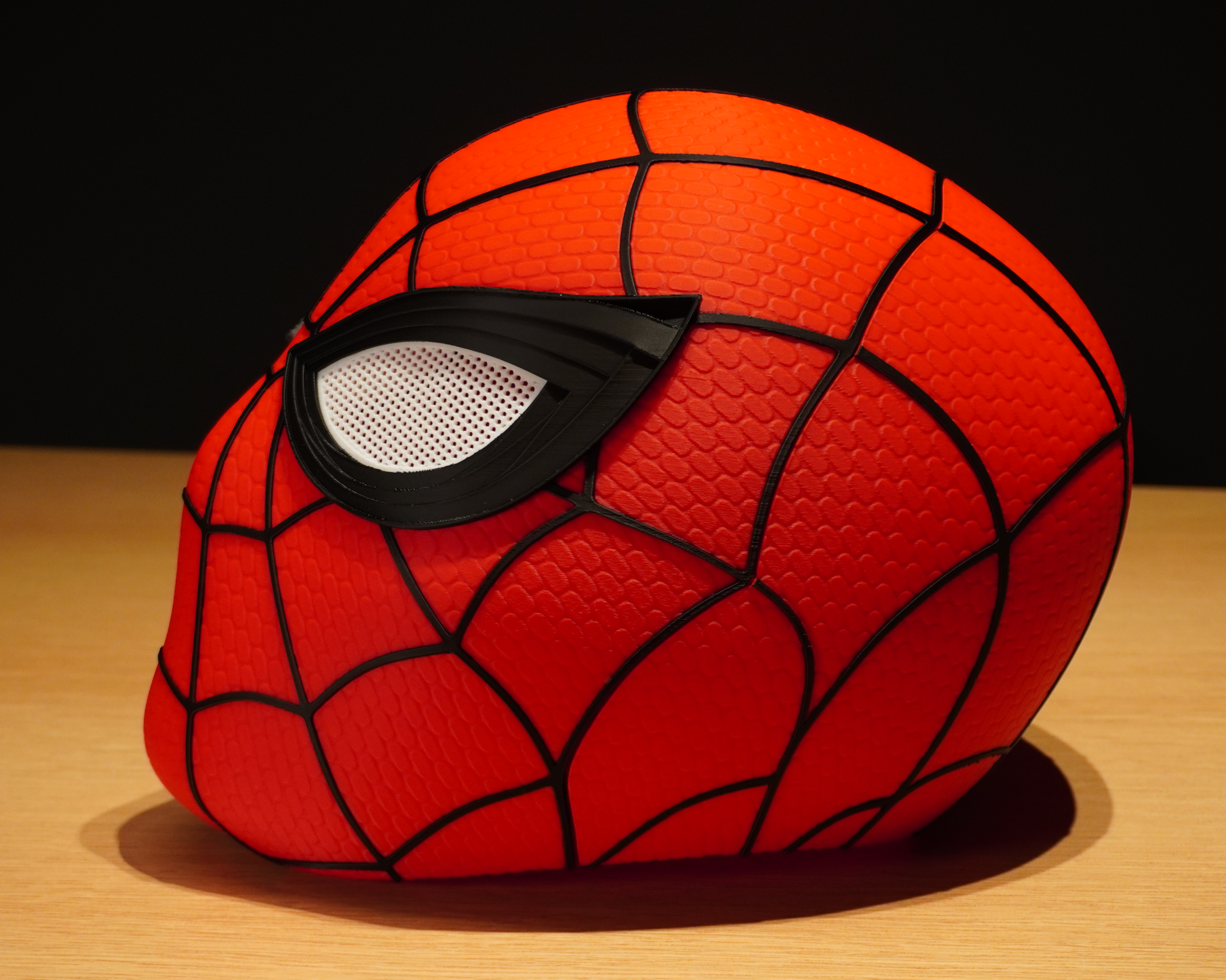 Side view of the Spider-Man mask showing the curved shell, layered web details, and eye assembly