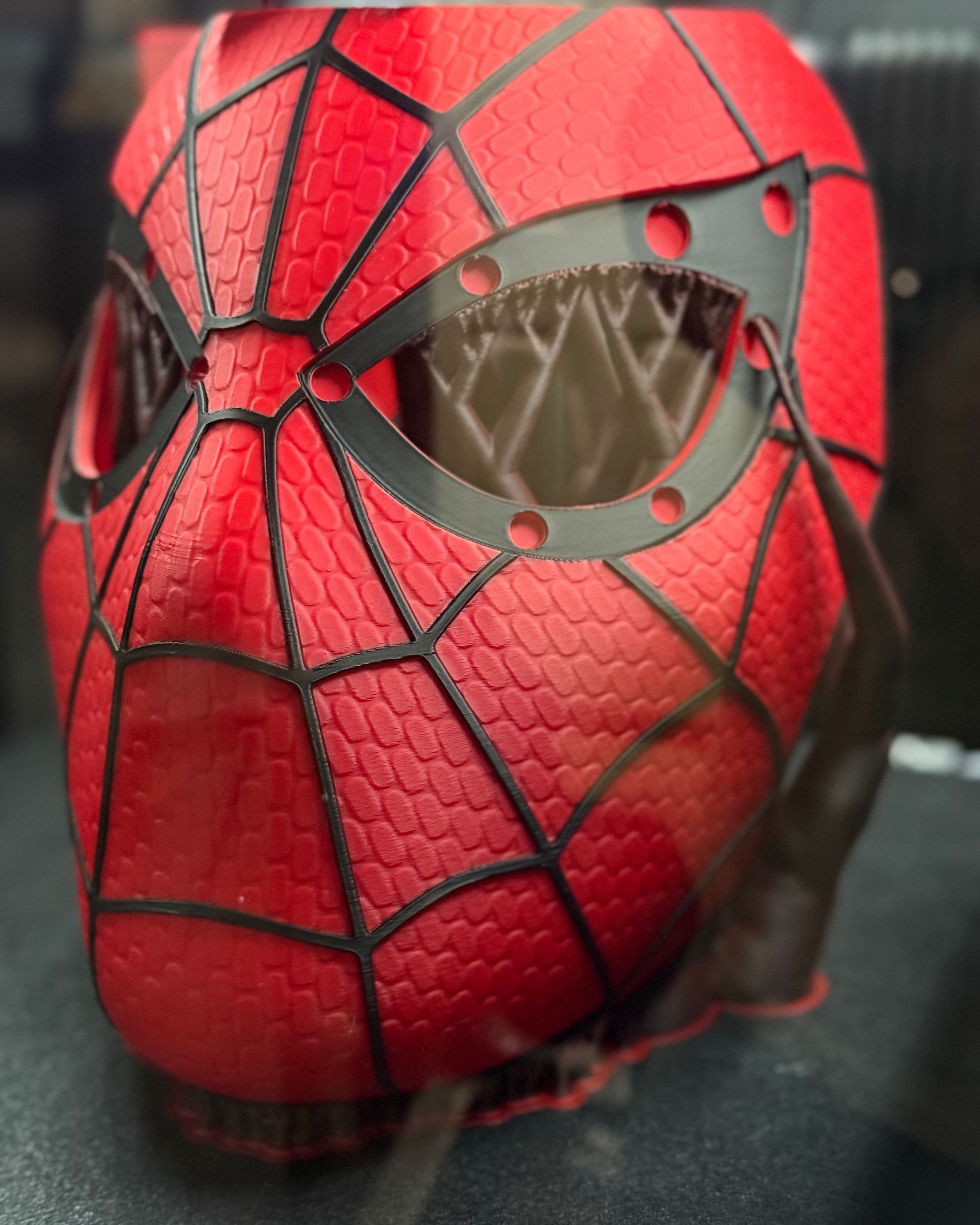 Close-up process view of the 3D-printed Spider-Man mask on the printer, showing the eye opening, magnet locations, and raised surface details