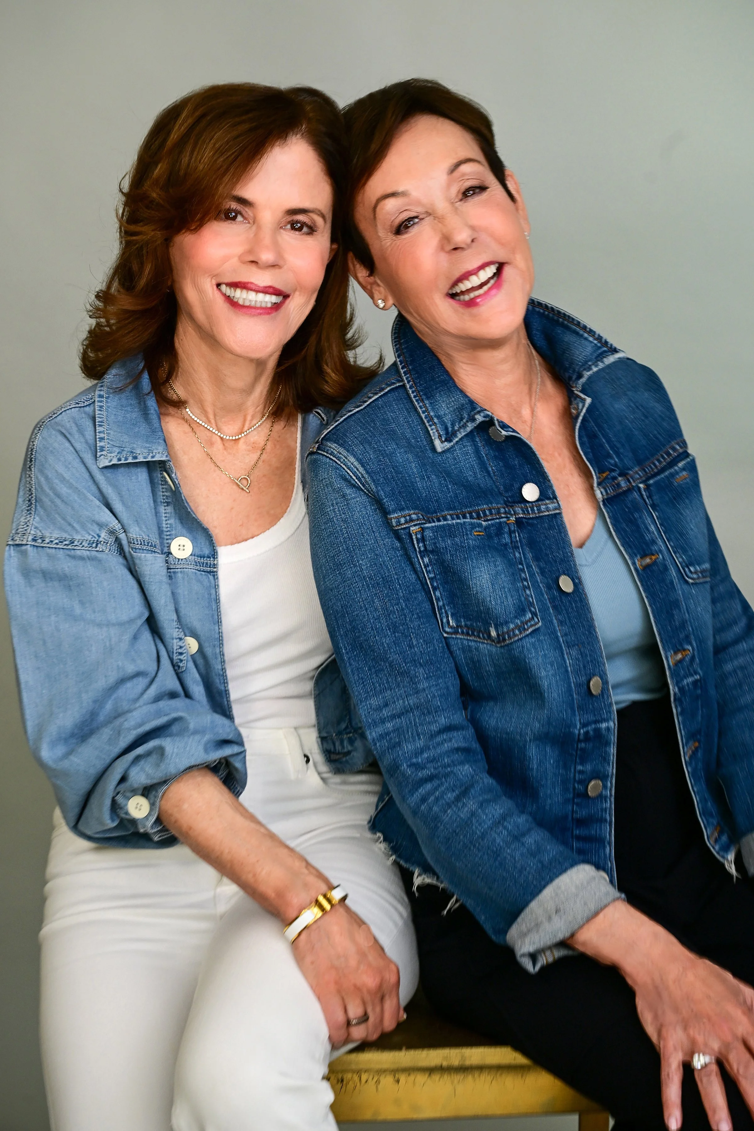 Pam Siegel and Leslie Zinberg smiling, wearing denim jackets, sitting close together against a plain background.