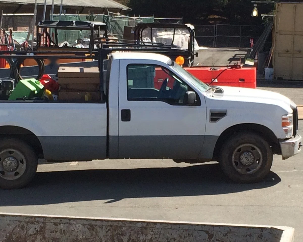 White work pickup with a ladder rack and tools in the bed parked in a contractor's yard
