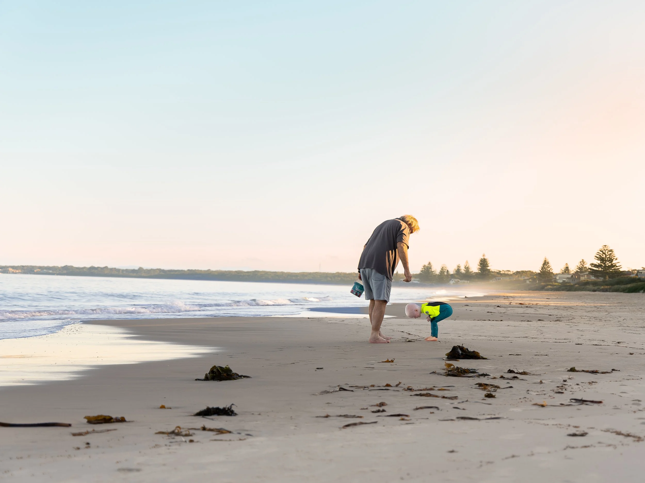 Grandfather walking along the beach with his grandson during a relaxed coastal family photoshoot with Monique Patmore Photography, capturing a candid moment as they explore the sand together.