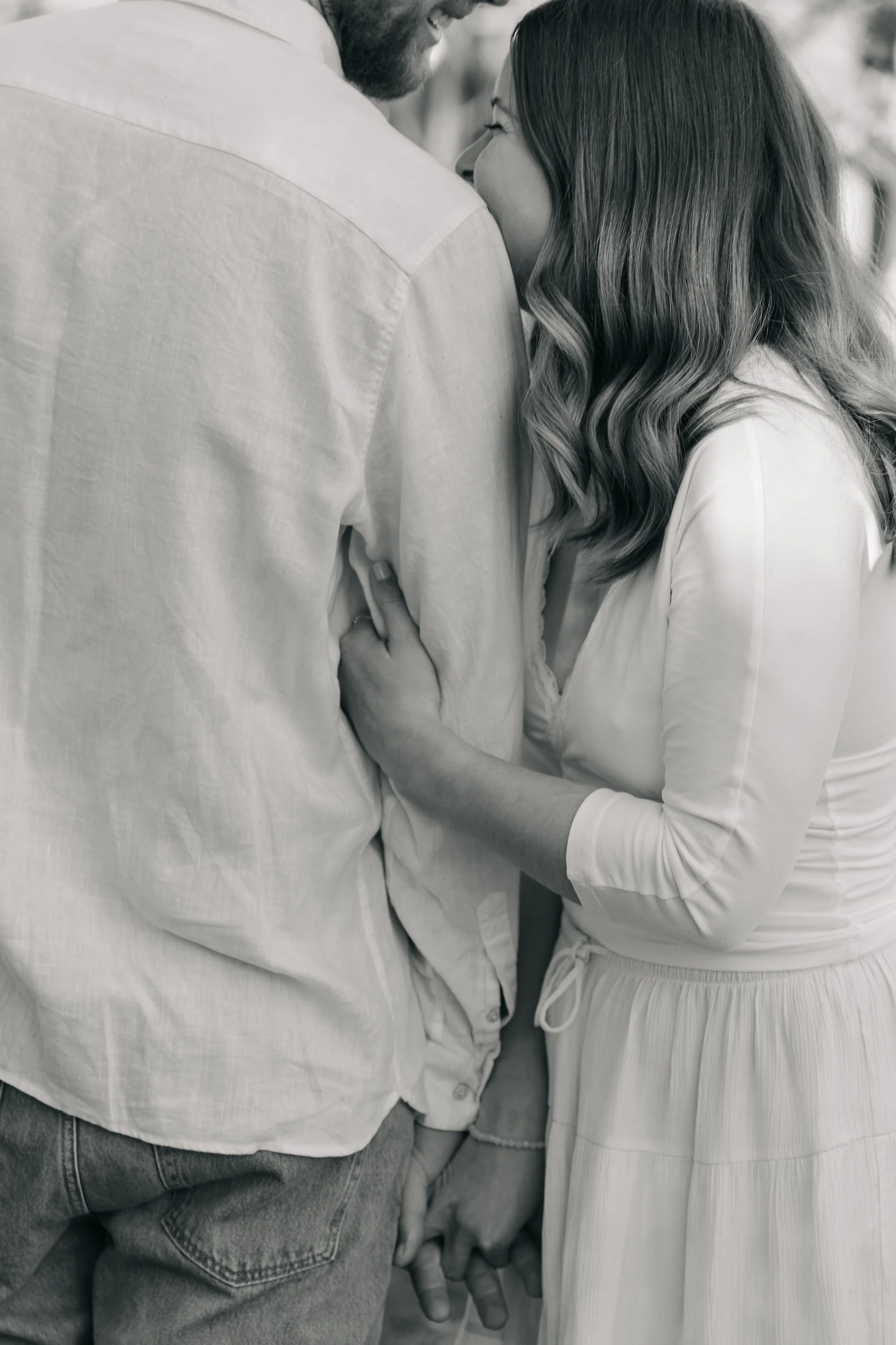 A black and white photo of a couple kissing, with only parts of their faces and hands visible.