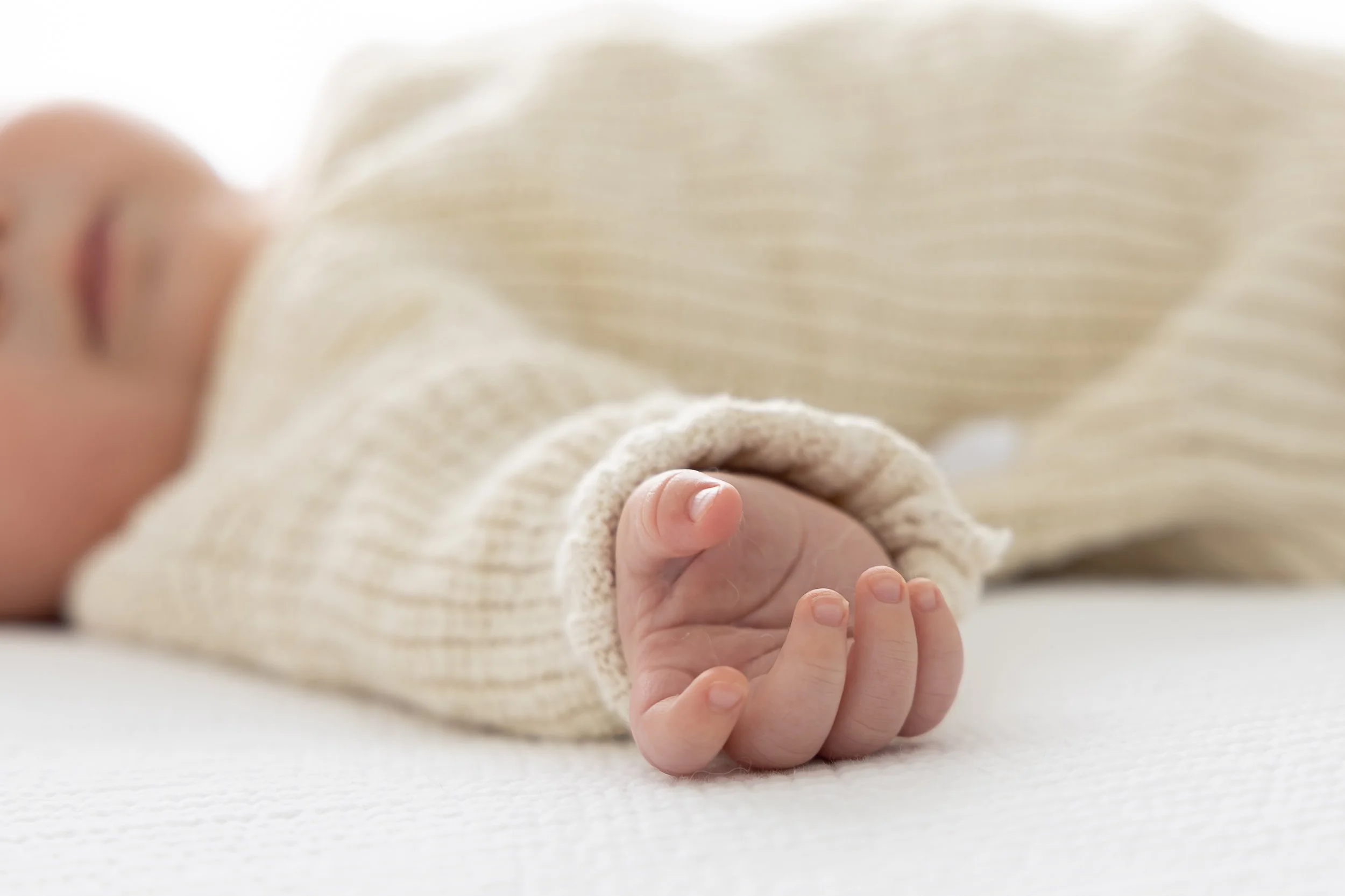 Close-up of a baby's tiny hand gripping an adult's finger, with the baby's face blurred in the background.