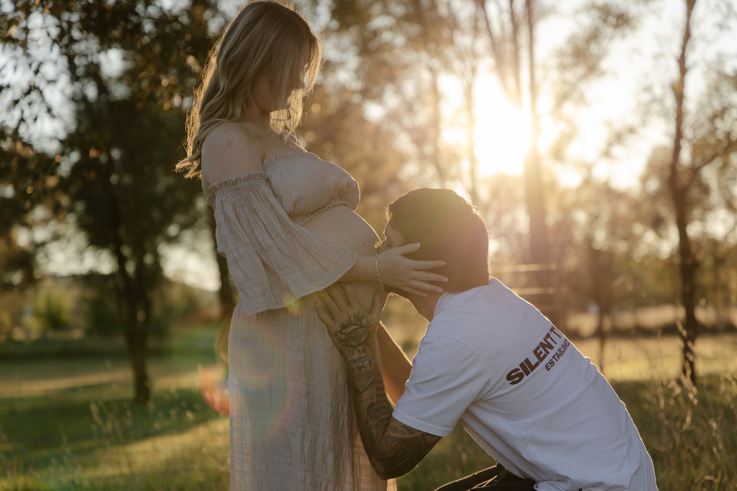 Expecting father kissing his pregnant fiance's bump during golden hour maternity photography session in Yass, NSW