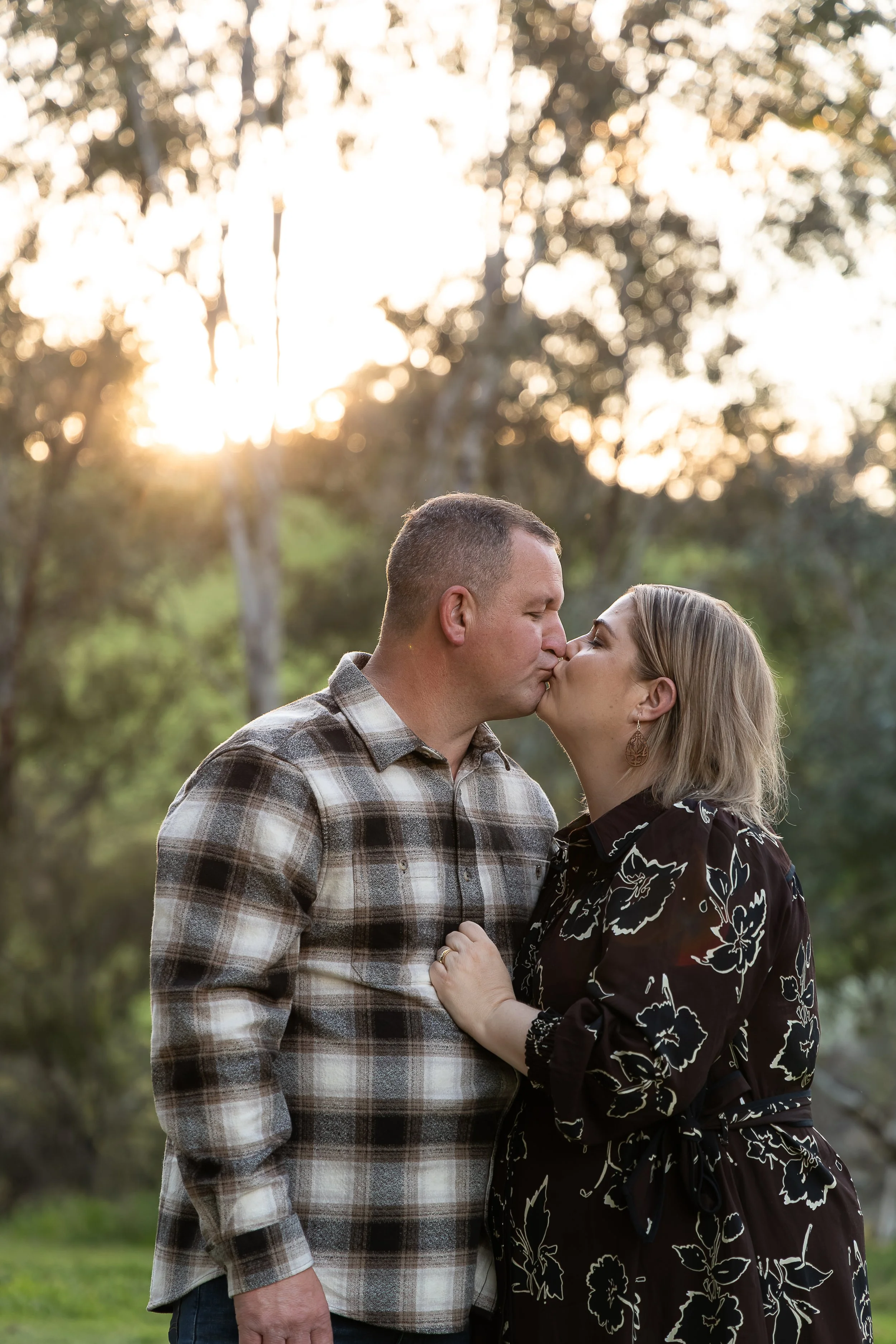 Golden hour family photography in Yass, NSW, capturing a beautiful candid moment as mum and dad share a kiss in the warm evening sunlight. Natural, heartfelt family photography by Monique Patmore Photography, serving Yass, Canberra and the surroundin