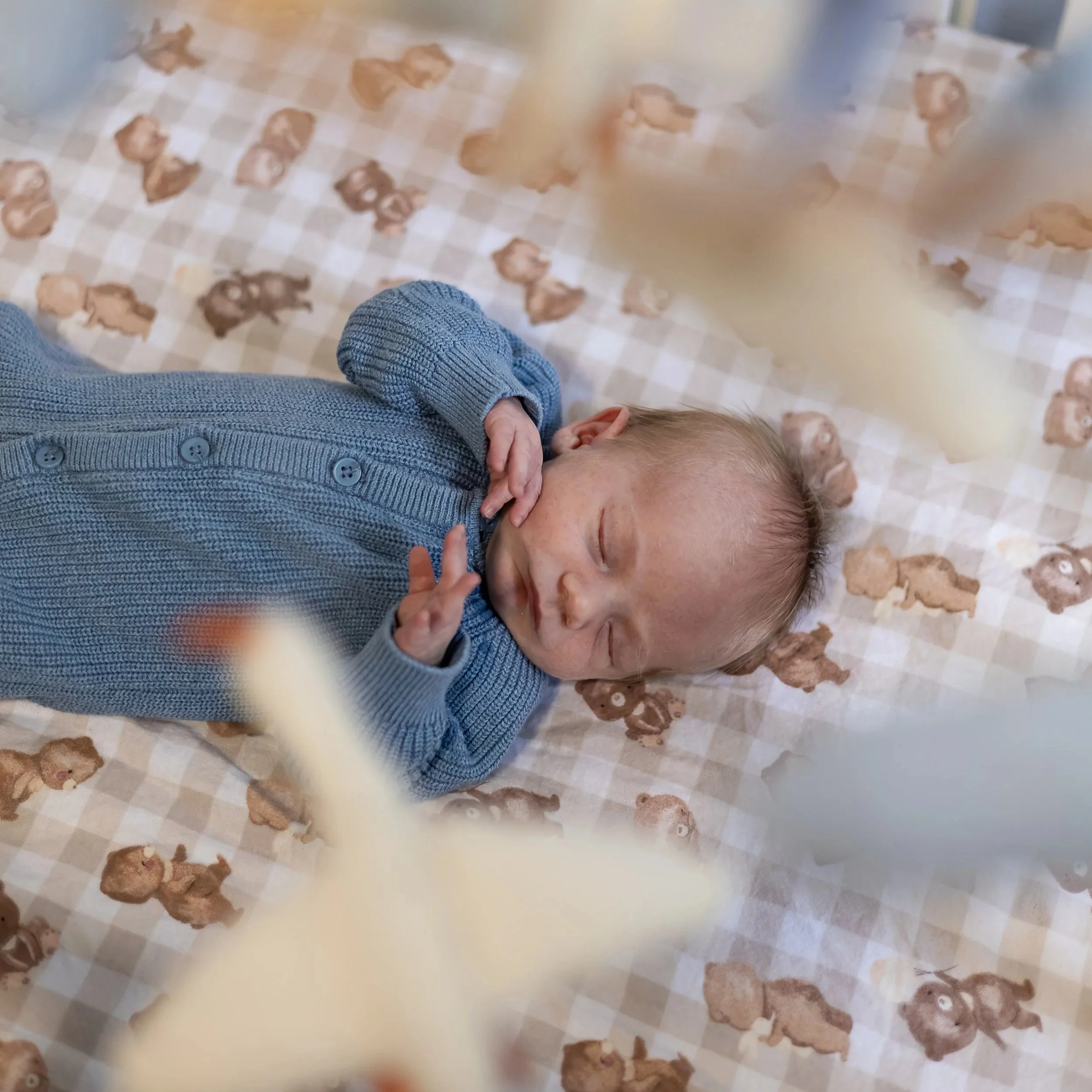 Newborn baby sleeping peacefully in their cot, photographed through a hanging mobile during an in-home newborn photography session in Canberra, ACT