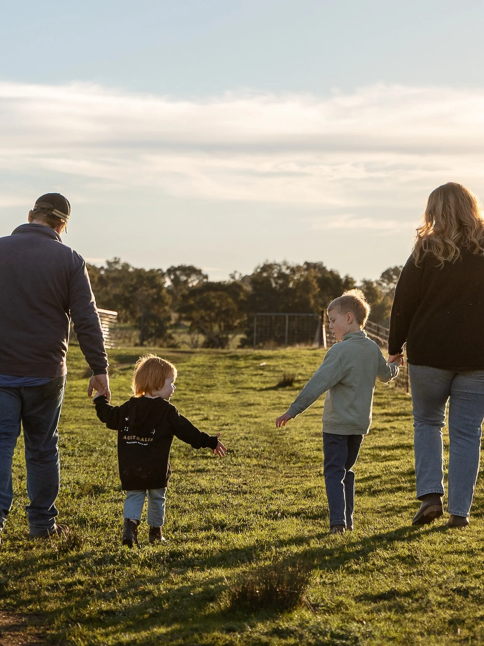 A group of children and adults walking in a park during sunset, holding hands and enjoying outdoor activity.