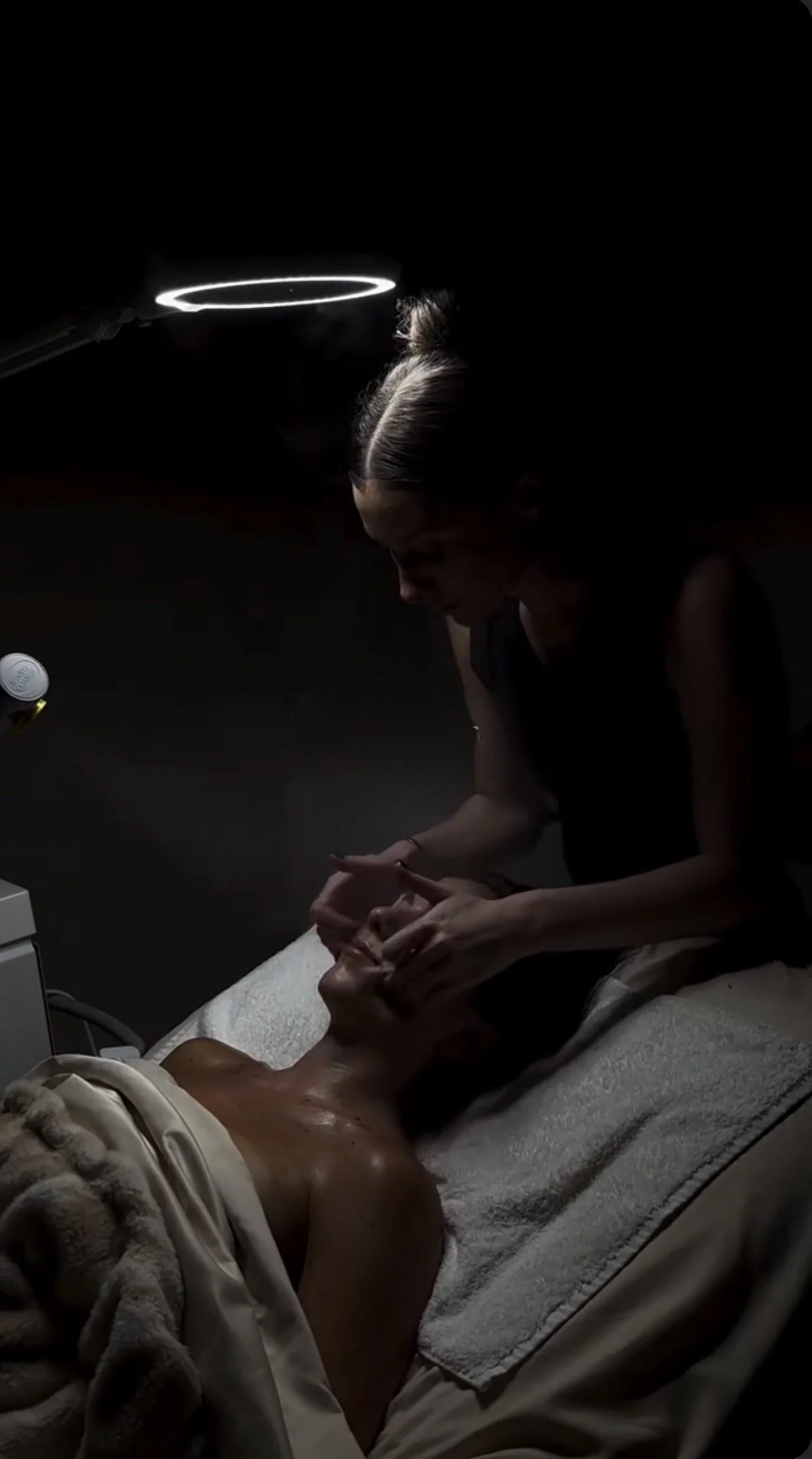A woman providing a massage to a person's foot in a dimly lit room with a halo-shaped light above her head.
