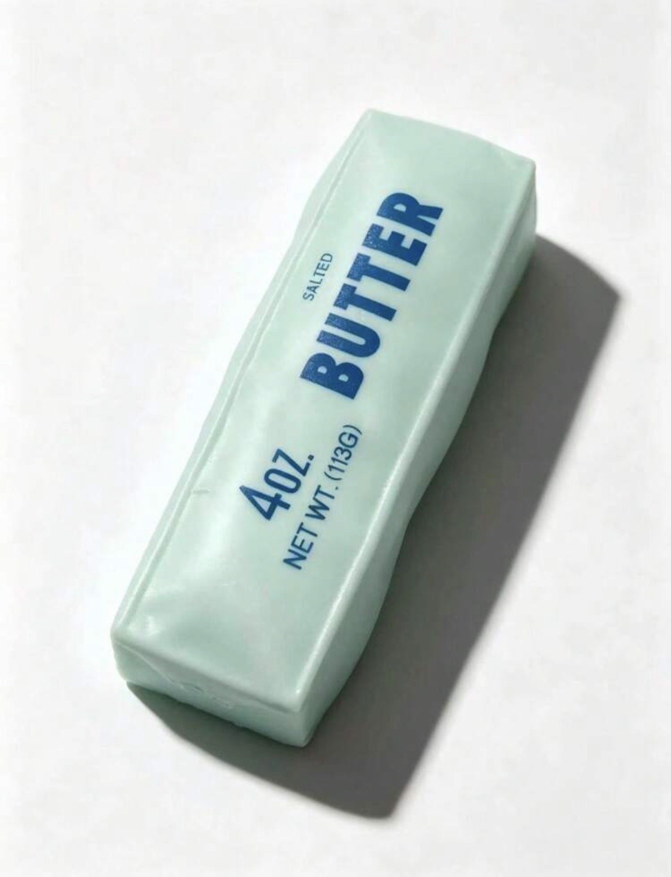 A stick of salted butter in a white wrapper with blue text, resting on a white surface, casting a shadow.