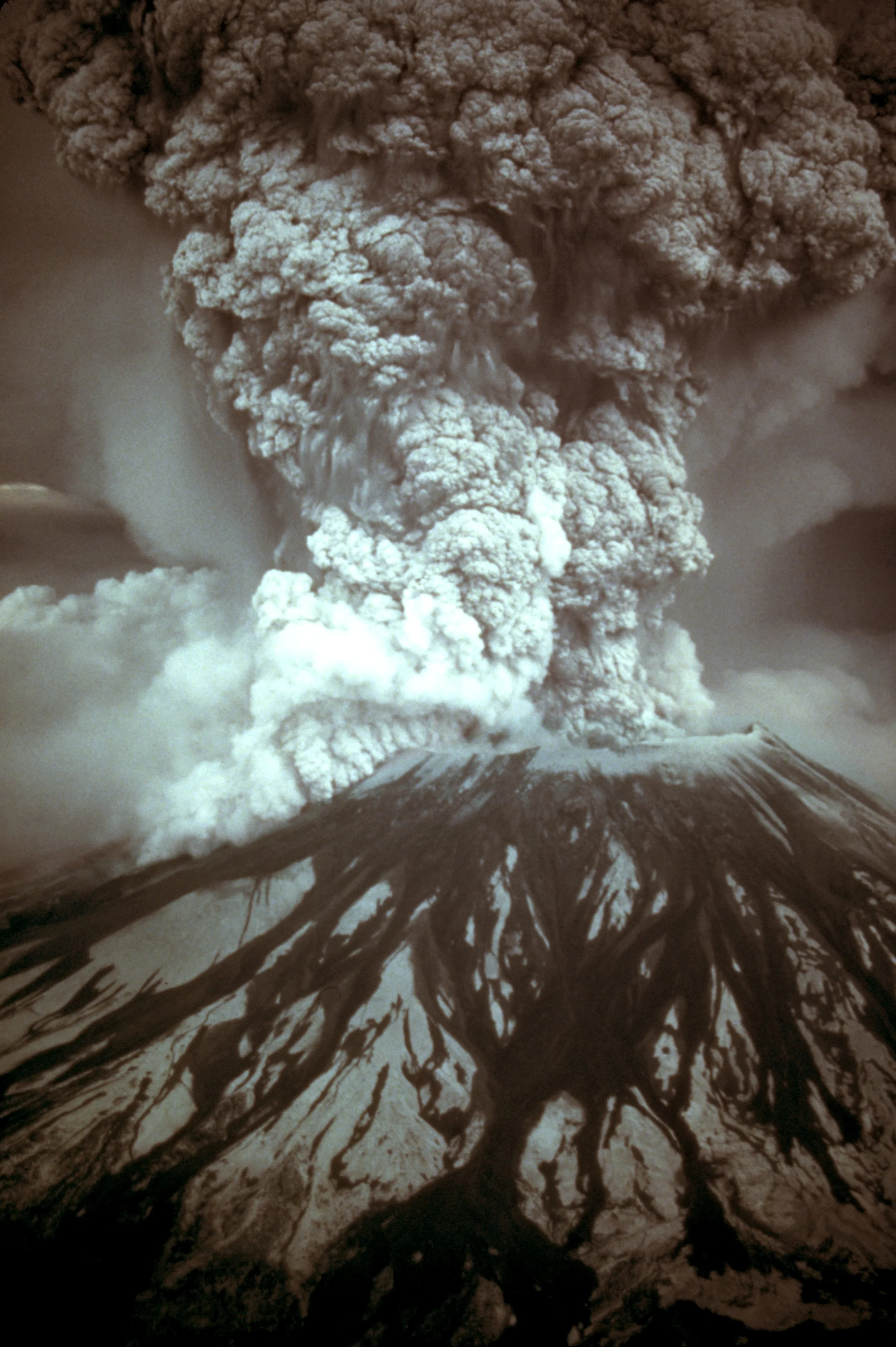 A volcanic eruption with a large ash cloud billowing into the sky, dark smoke, and fiery lava flows reaching down the sides of the volcano.