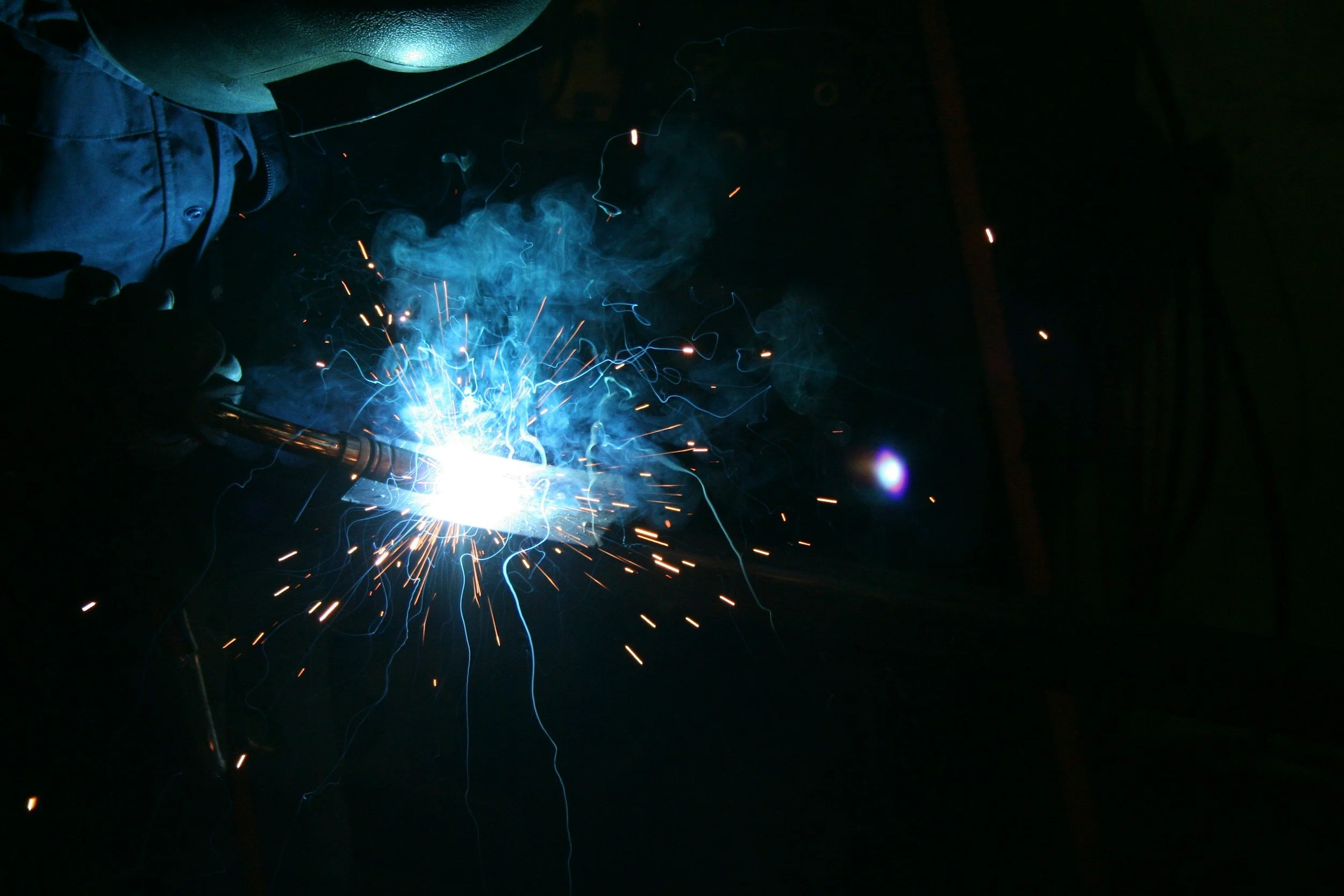 A person welding metal in a dark environment, with bright sparks and blue smoke.