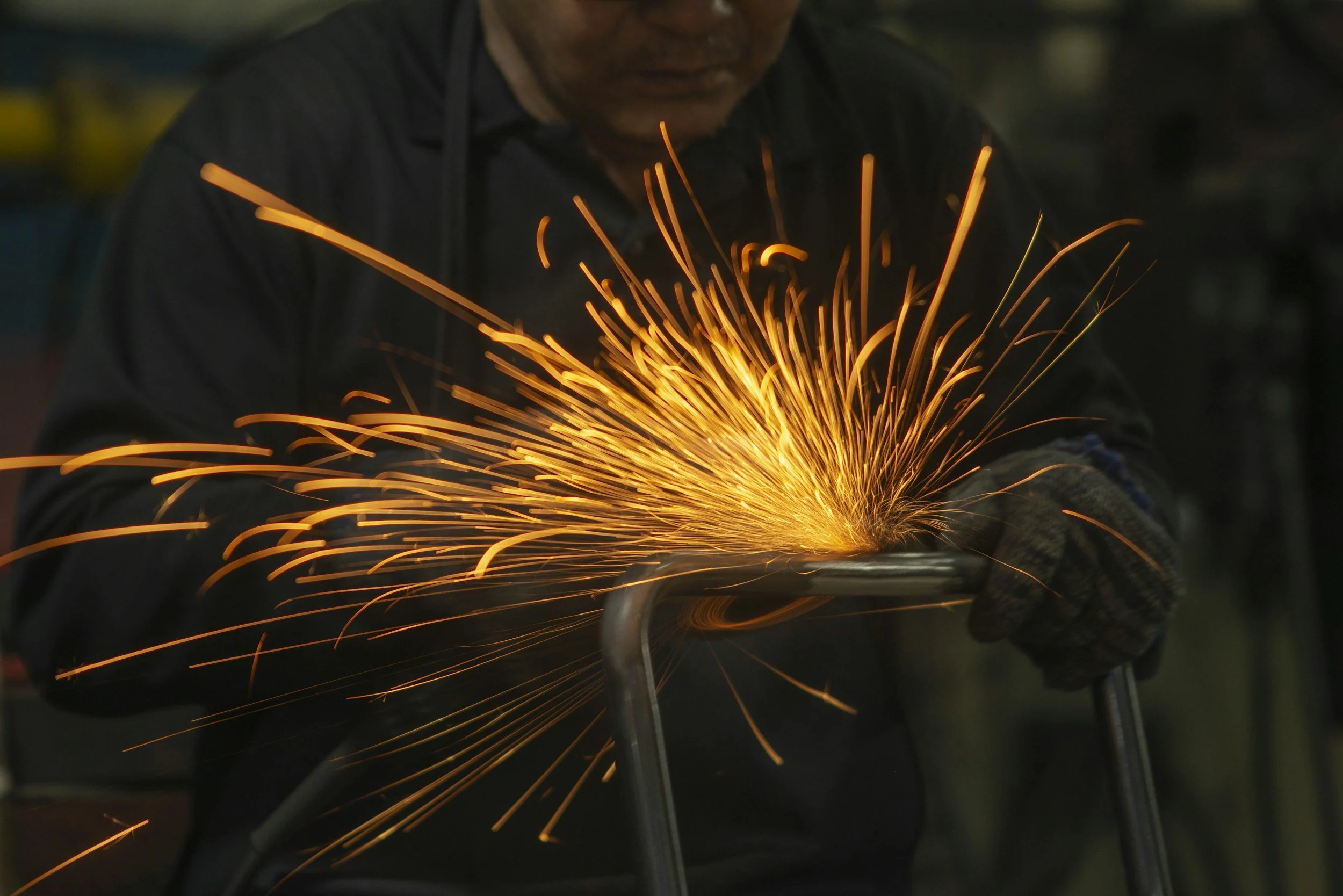 A person grinding metal while sparks fly around in a workshop or industrial setting.