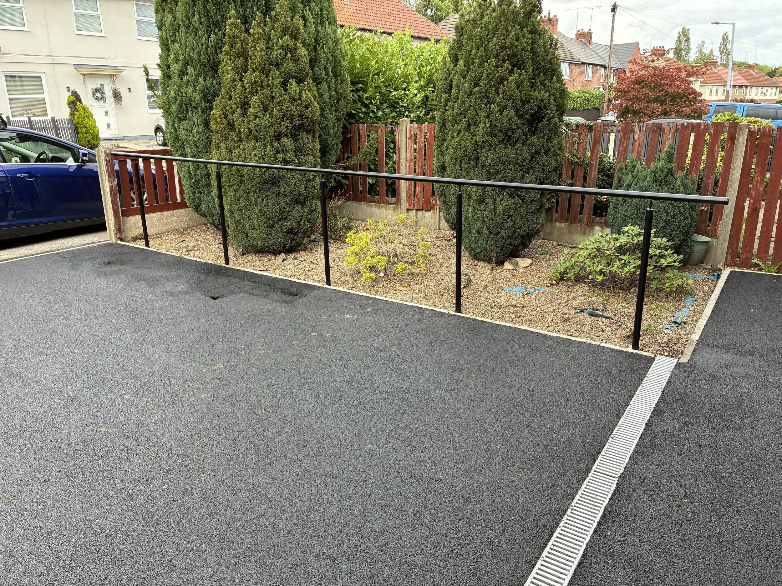 Black steel handrail fitted alongside a sloping driveway, providing support on the approach to the house.